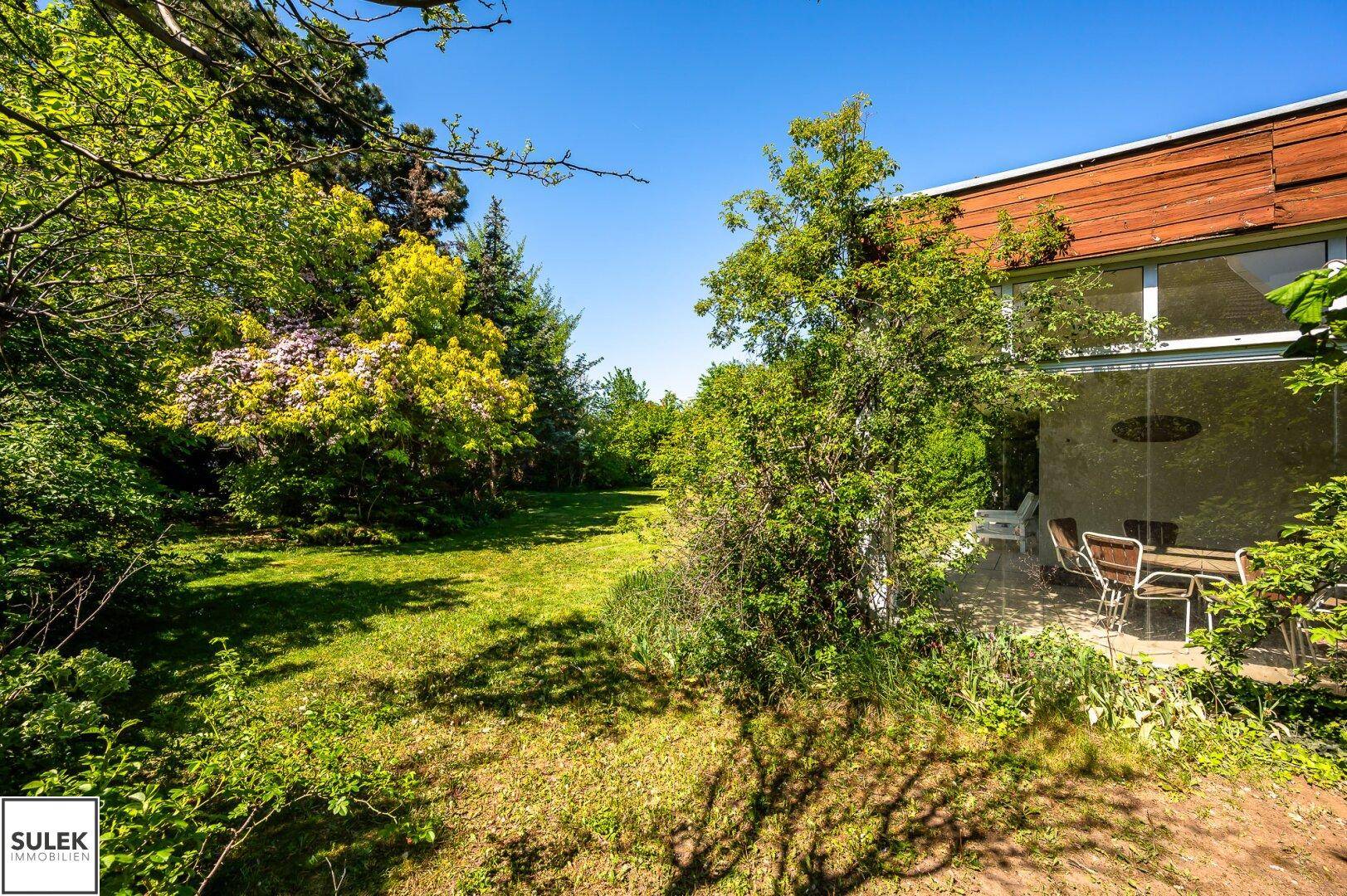 Großer Gartenbereich mit Rasen und angrenzendem Wintergarten oder überdachter Terrasse.