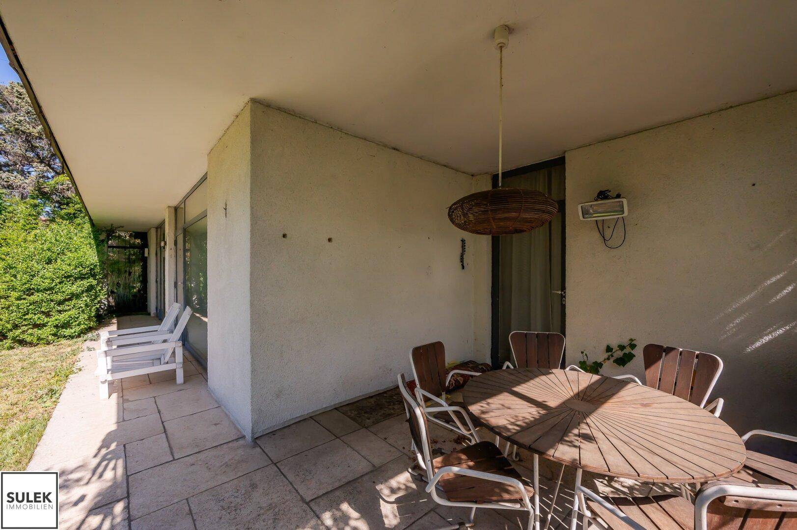 Eine überdachte Terrasse mit Steinfliesen und einem Holztisch mit Stühlen für Mahlzeiten im Freien.