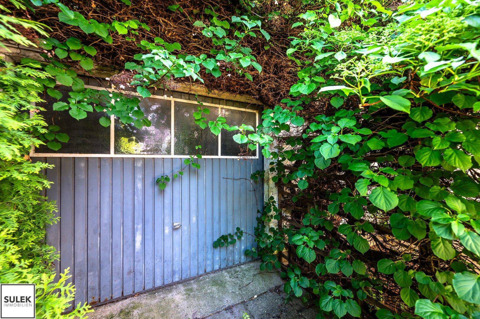 Eine Garagentür, die teilweise von dichtem Grün und Kletterpflanzen bedeckt ist.