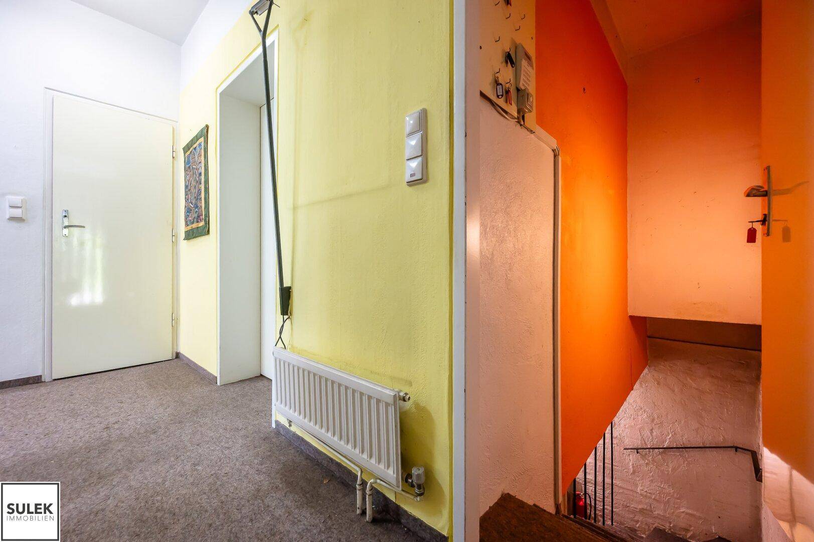 Flur mit gelben Wänden und Treppenabgang, in renovierungsbedürftigem Zustand.