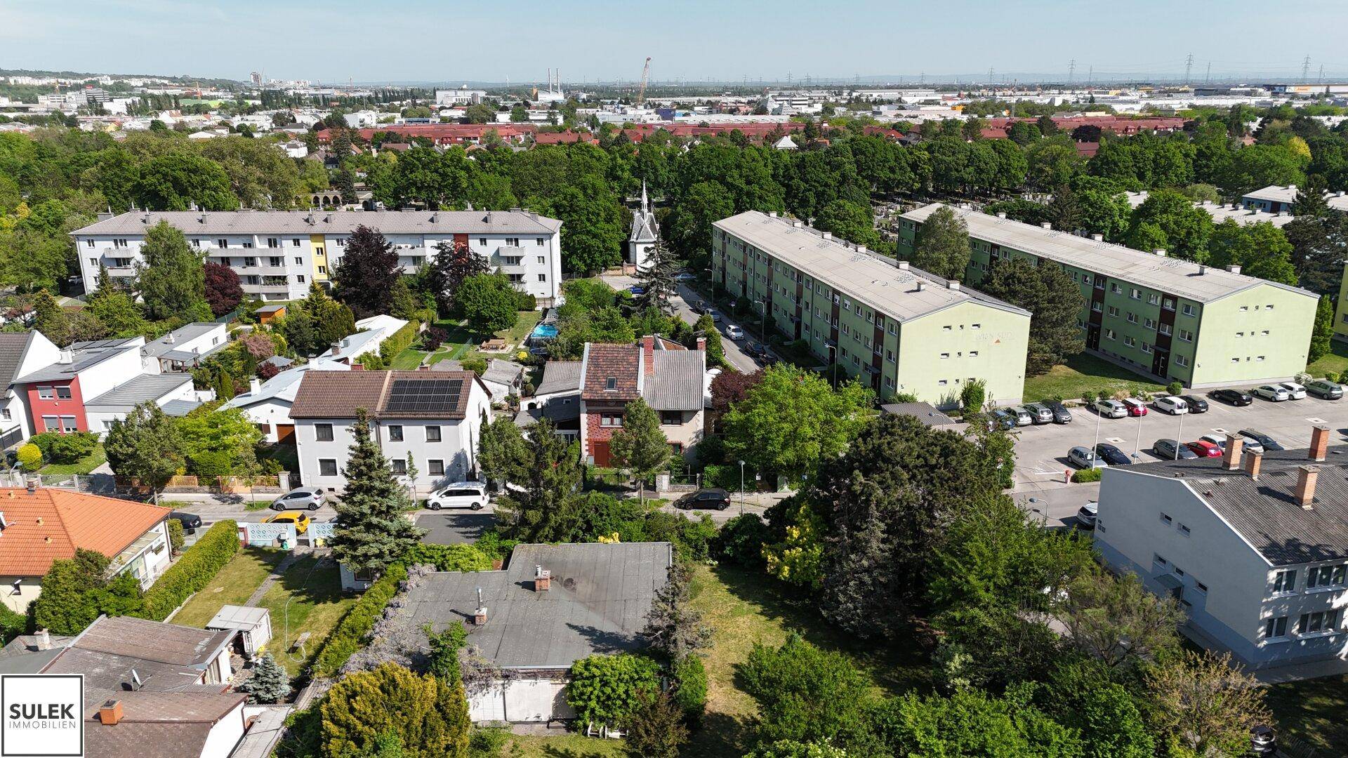 Luftaufnahme einer gemischten Wohngegend mit Einfamilienhäusern und Mehrfamilienhäusern, umgeben von viel Grün.