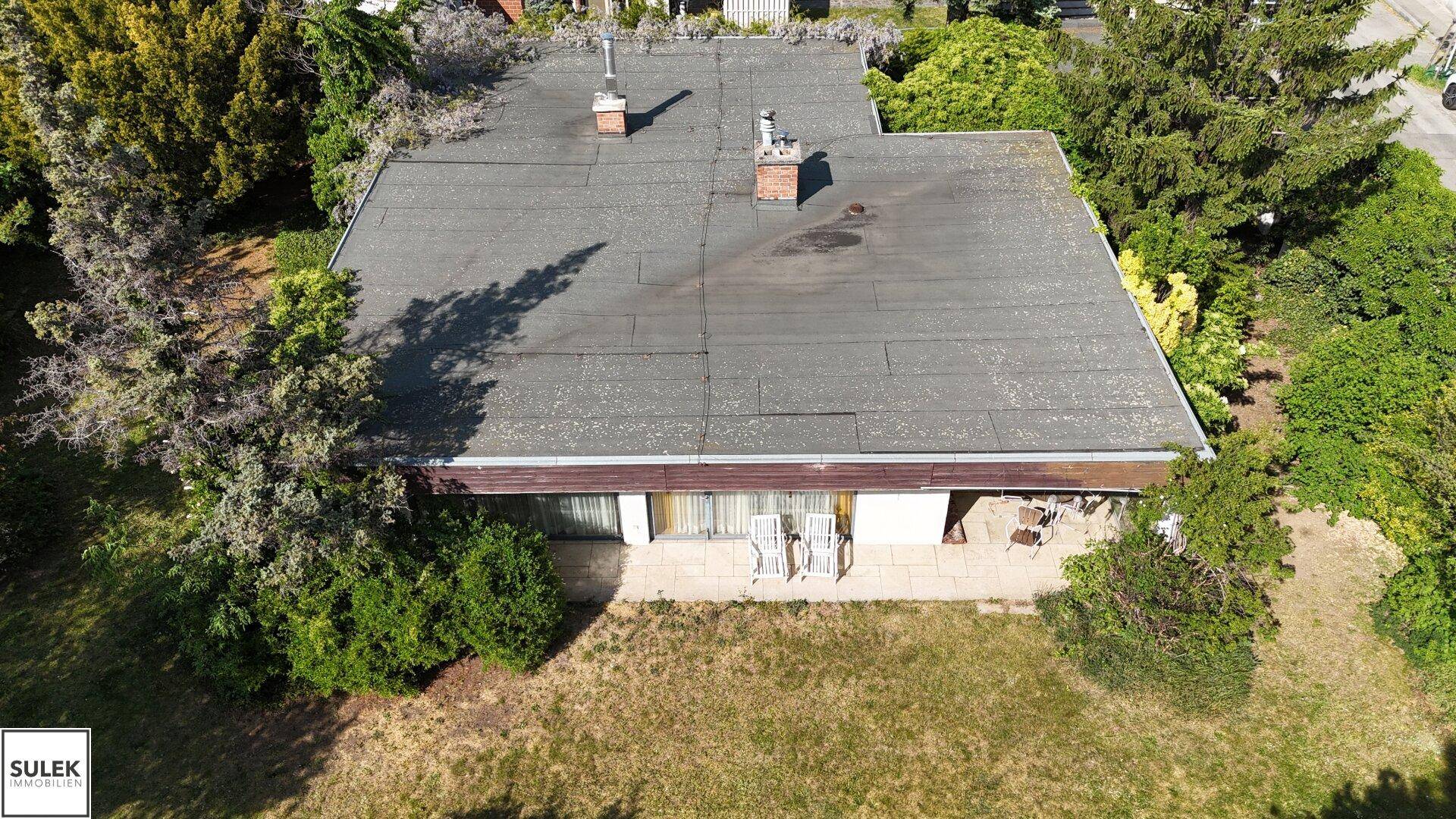 Rückseite des Hauses mit großer Terrasse, Gartenmöbeln und Blick ins Grüne, ideal zum Entspannen.