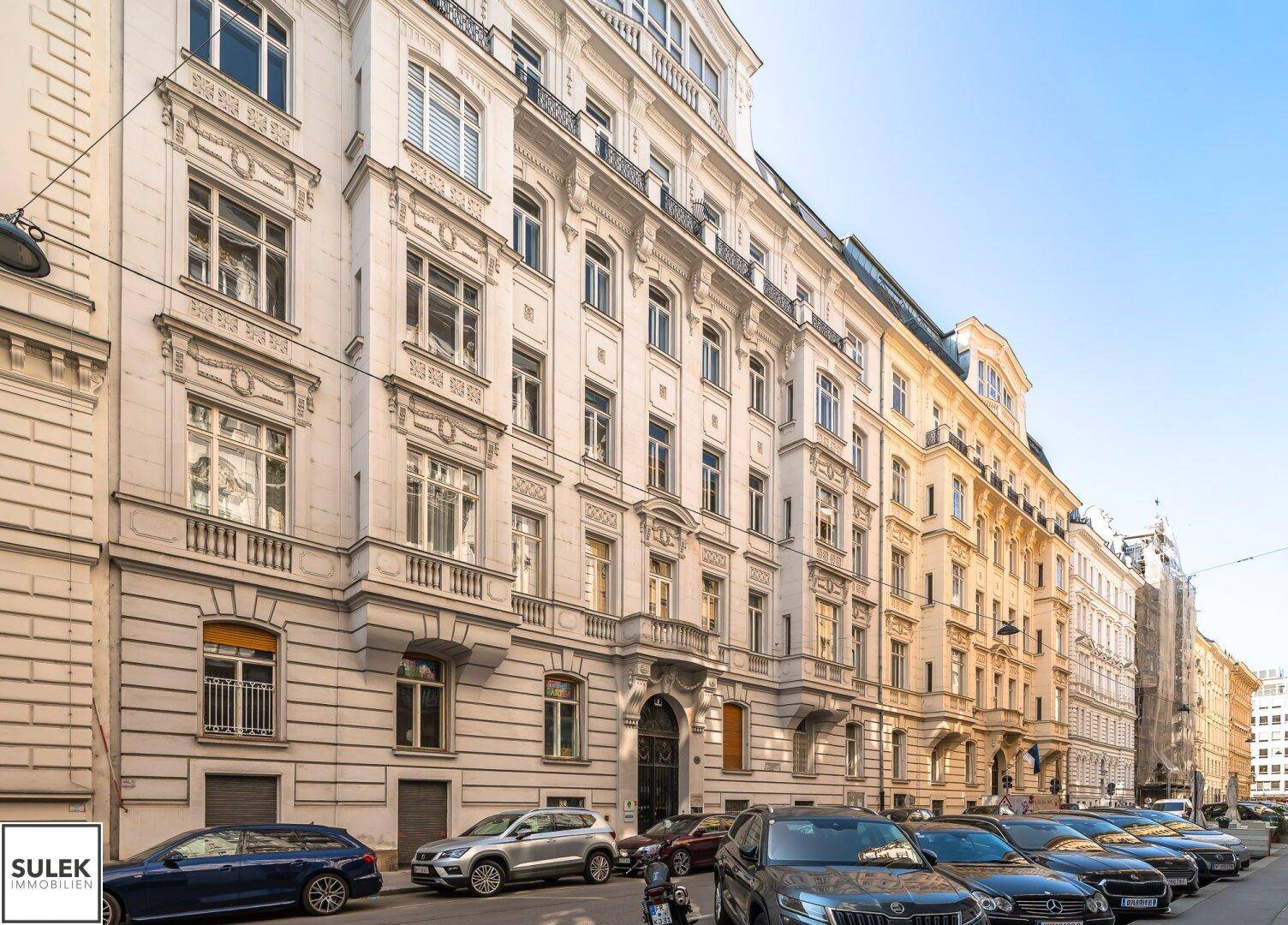 Historisches Gebäude mit reich verzierter Fassade und parkenden Autos auf der Straße.
