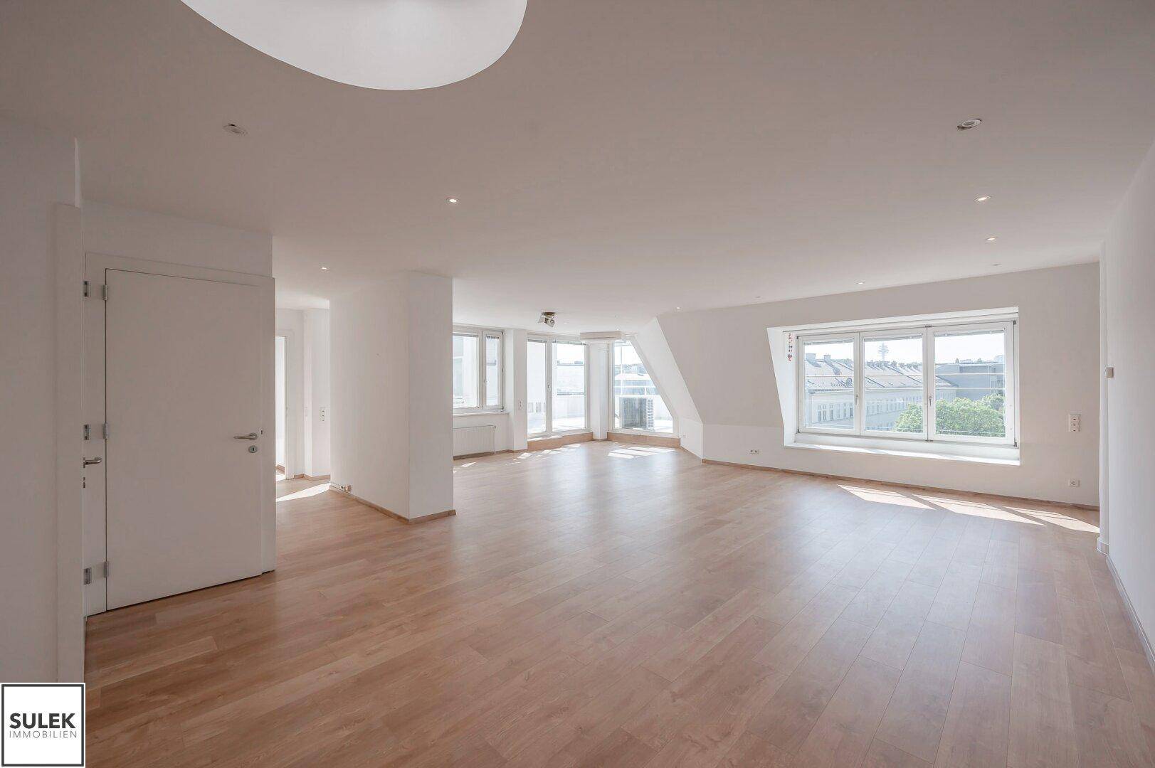 Geräumiger, heller Wohnbereich mit Parkettboden, vielen Fenstern und moderner Beleuchtung.
