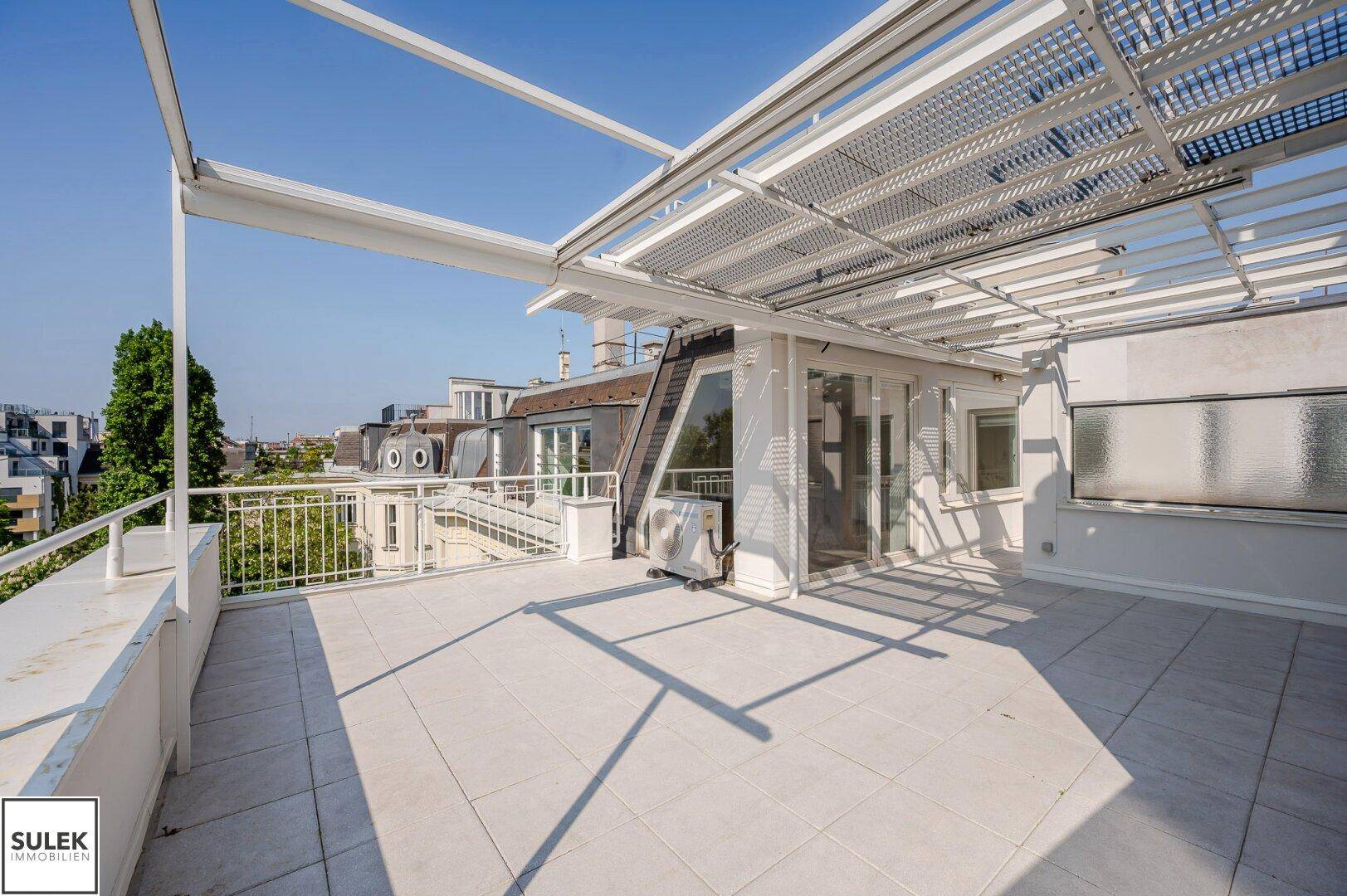Weitläufige Dachterrasse mit Fliesenboden, Pergola und Blick auf die umliegenden Dächer.