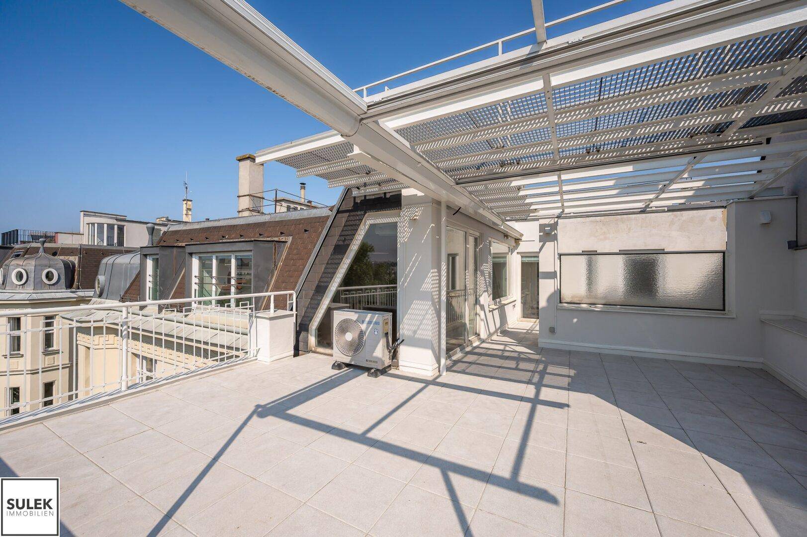 Große Dachterrasse mit Fliesenboden, Pergola und weitem Blick über die Stadt.