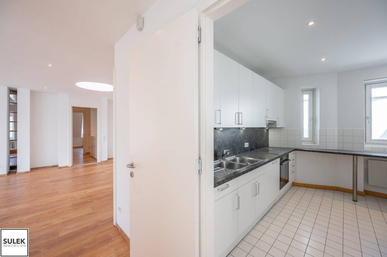 Moderne Einbauküche mit weißen Schränken, dunkler Arbeitsplatte und Fliesenboden.