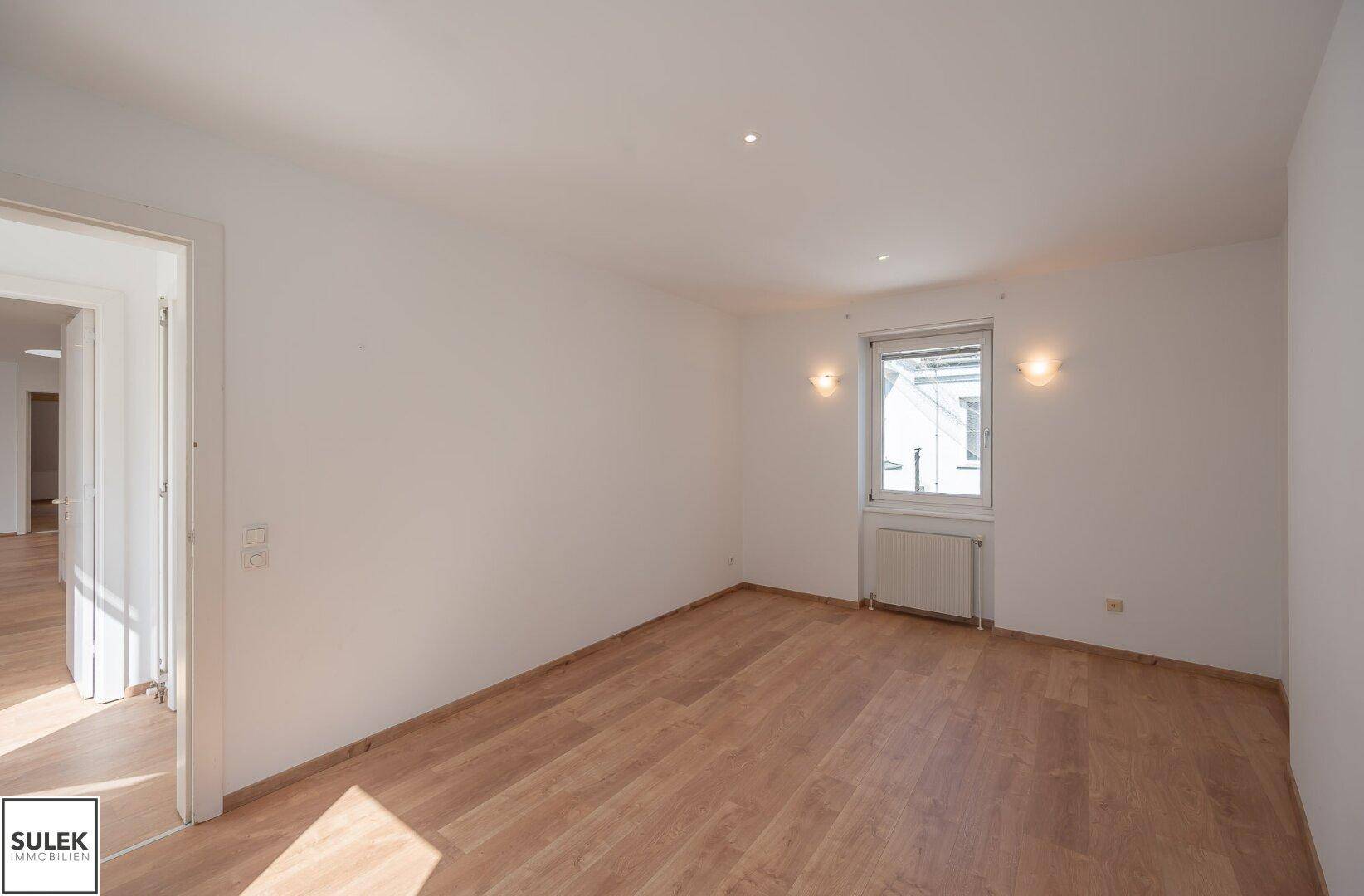 Helles Schlafzimmer mit Parkettboden, Fenster und direkter Verbindung zum Wohnbereich.