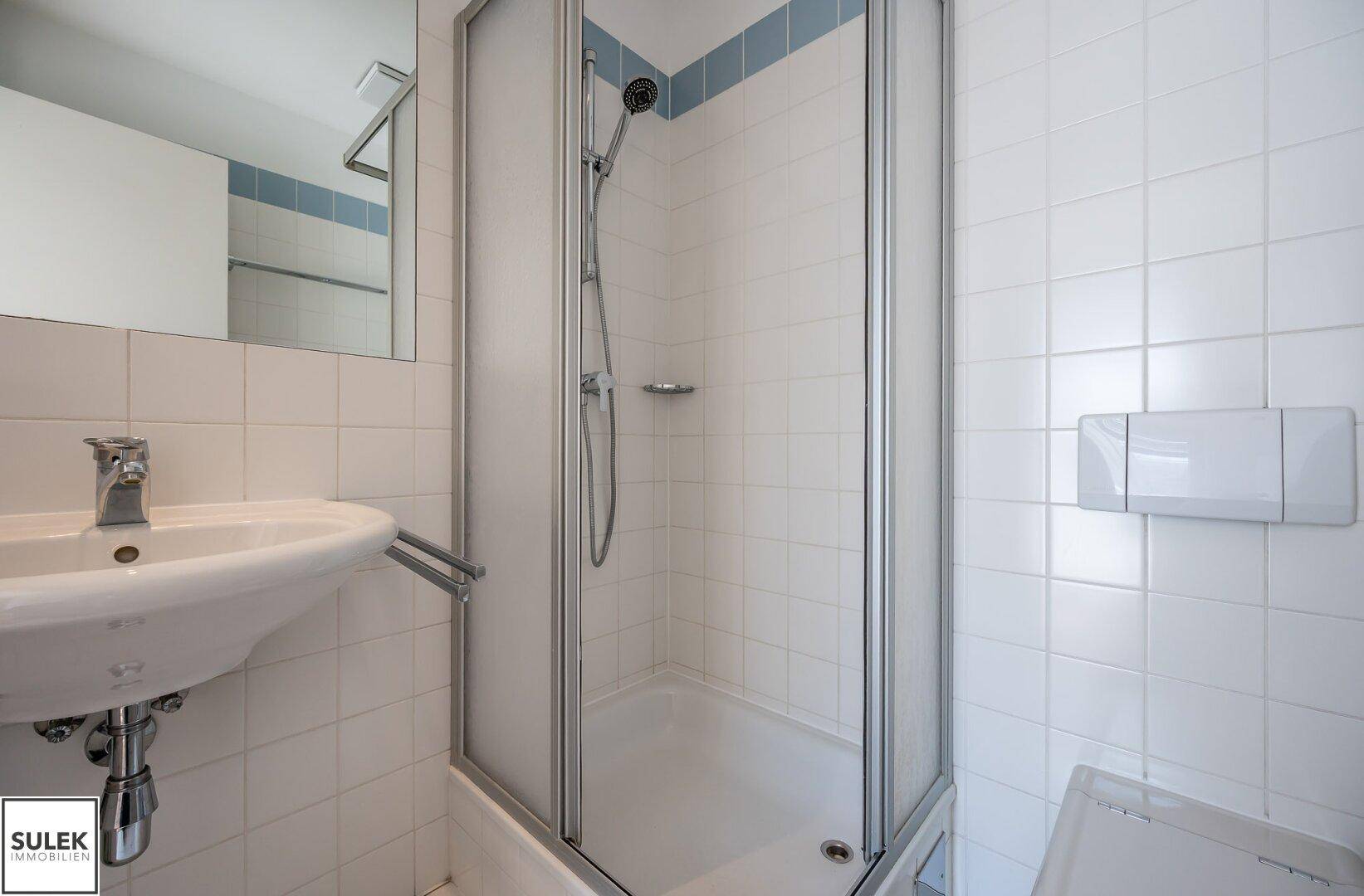 Helles Badezimmer mit Dusche, Waschbecken und weißen Fliesen.