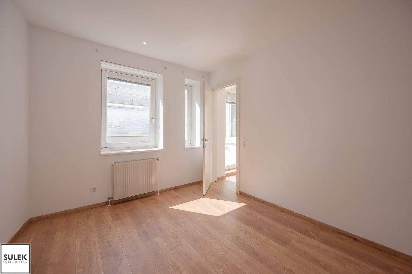 Helles Schlafzimmer mit Parkettboden und zwei Fenstern für viel Tageslicht.
