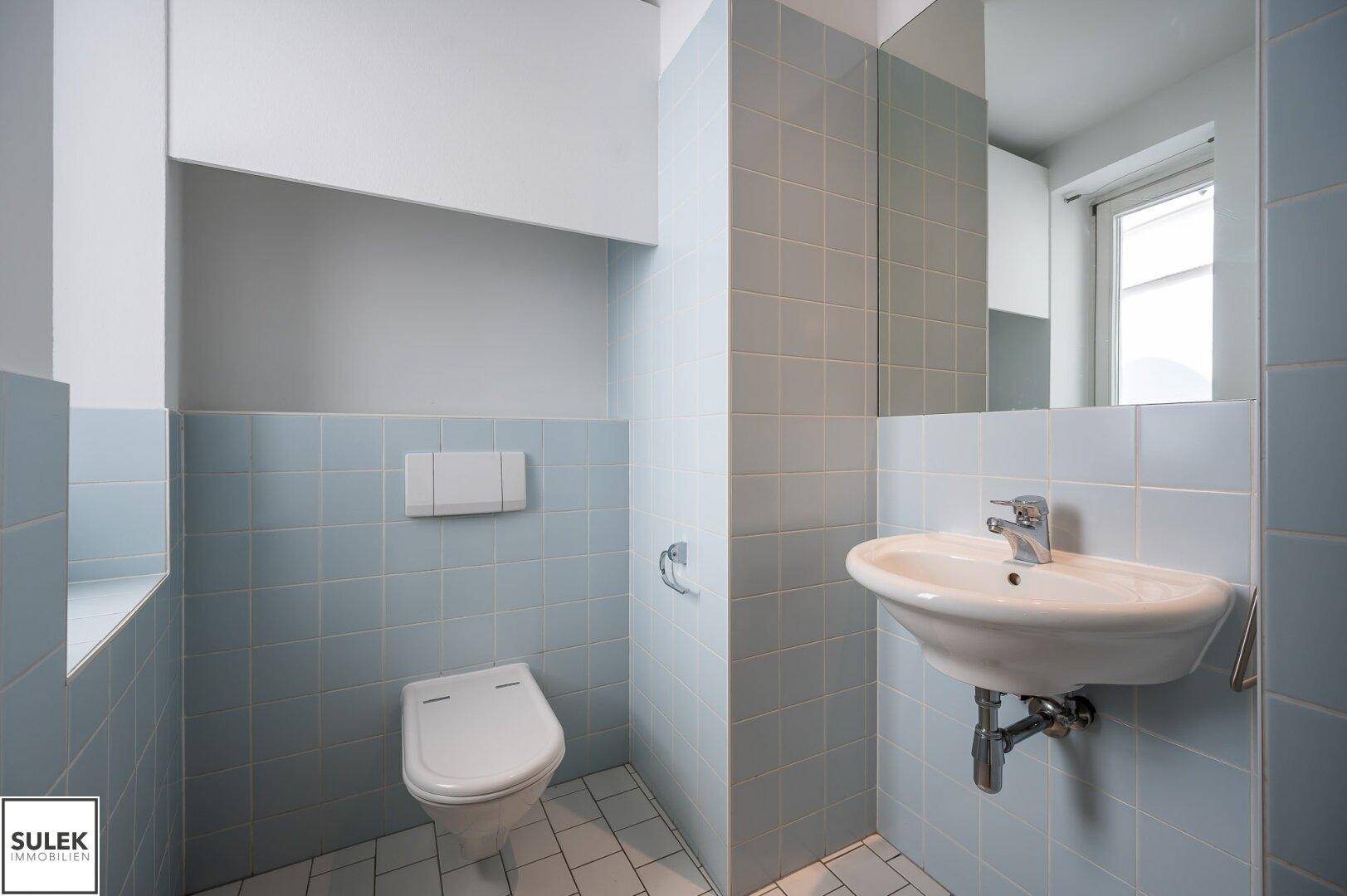 Modernes Gäste-WC mit hellblauen Fliesen, Waschbecken und wandhängendem WC.