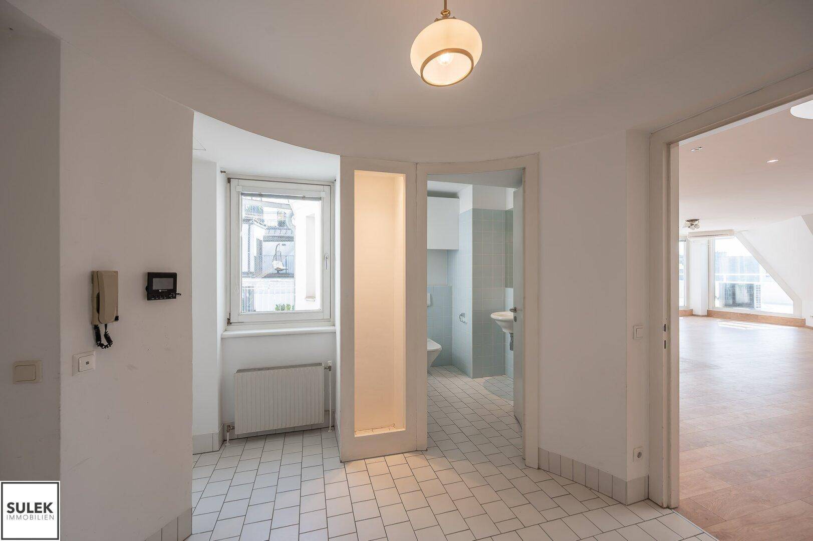 Heller Flur mit Fliesenboden, Fenster und Zugang zum Gäste-WC und den Wohnbereichen.