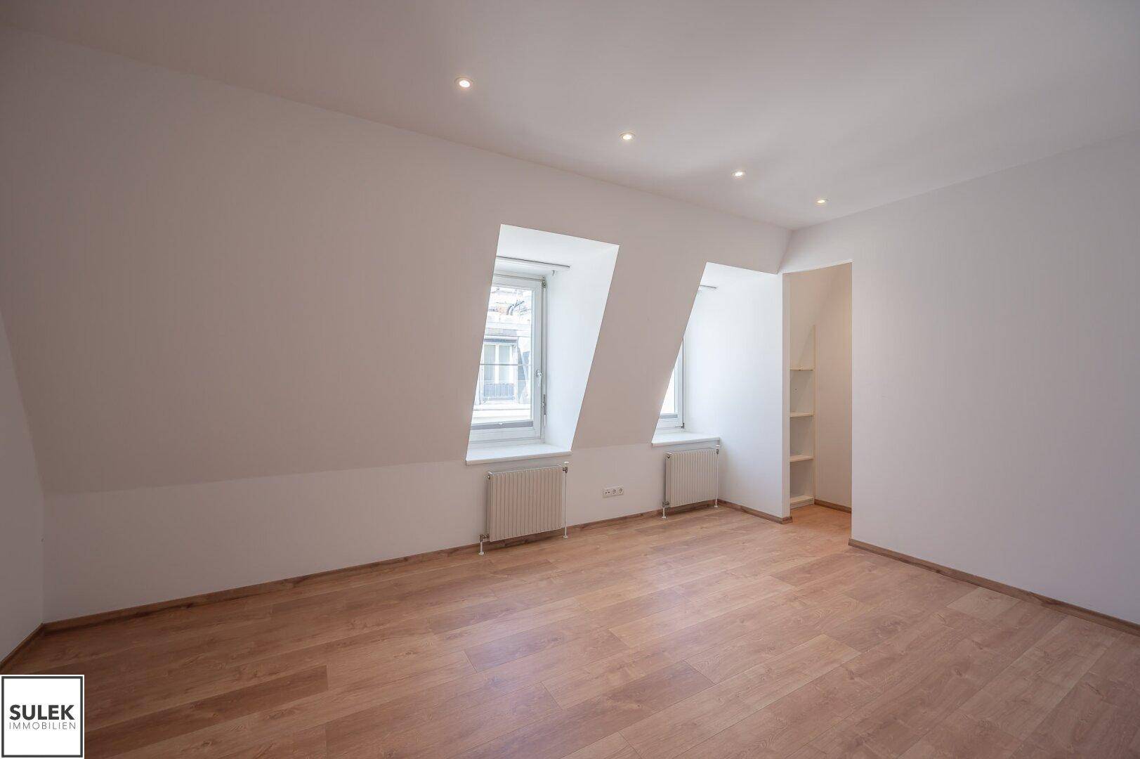 Geräumiges Schlafzimmer im Dachgeschoss mit schrägen Wänden und zwei Fenstern.