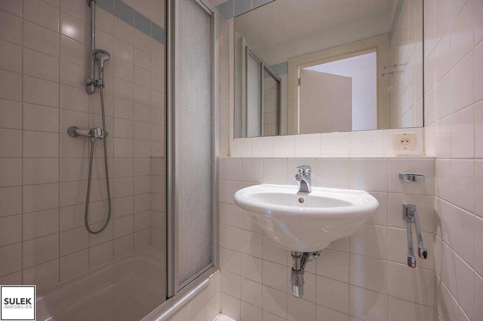 Kleines Badezimmer mit Dusche, Waschbecken und weißen Fliesen.