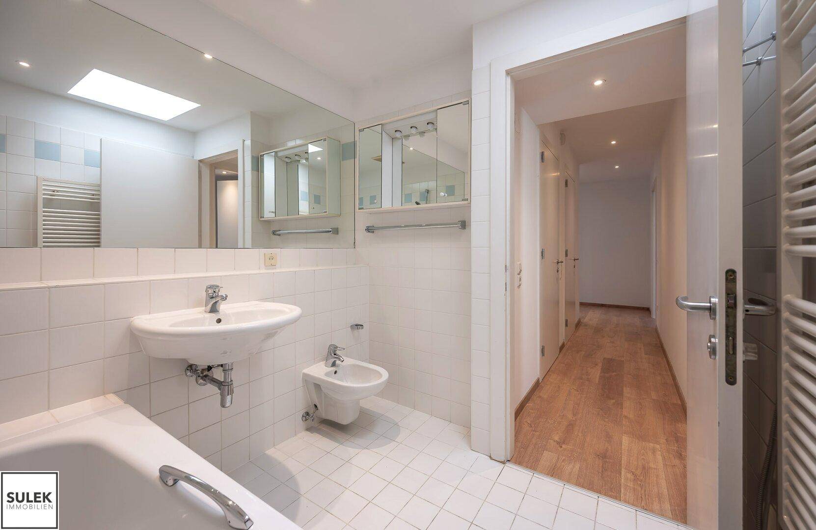 Geräumiges Badezimmer mit Badewanne, Waschbecken, Bidet und Zugang zum Flur.