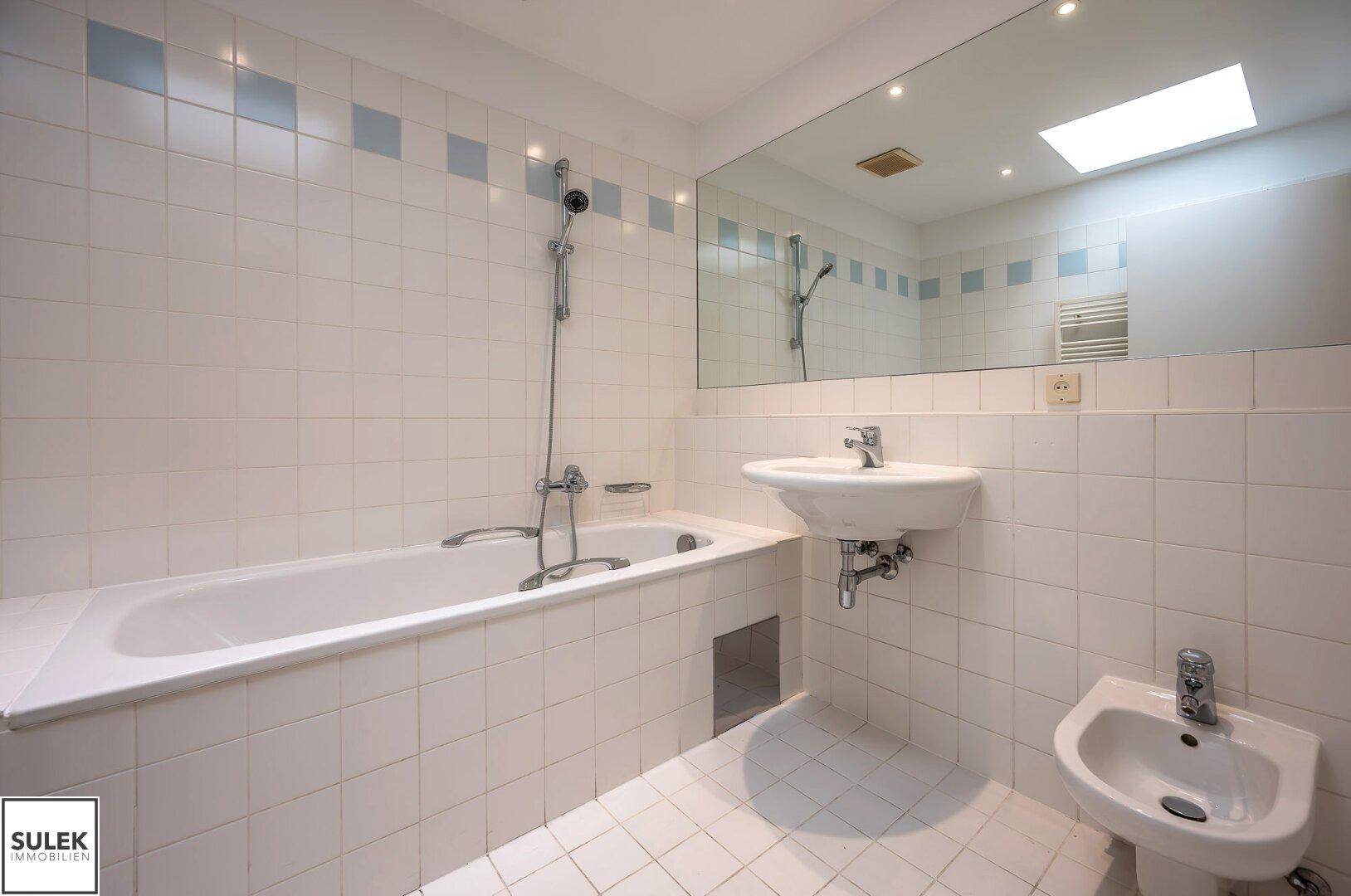 Helles Badezimmer mit Badewanne, Waschbecken, Bidet und weißen Fliesen.