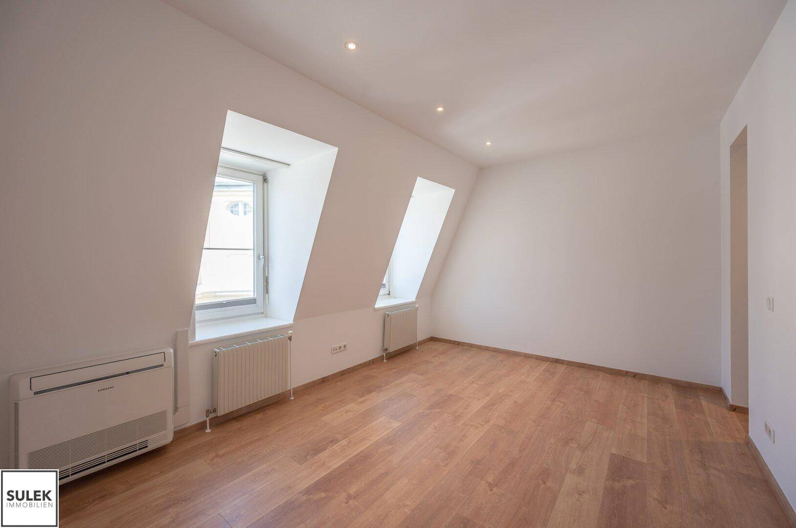 Helles Schlafzimmer im Dachgeschoss mit schrägen Wänden, Fenstern und Klimaanlage.