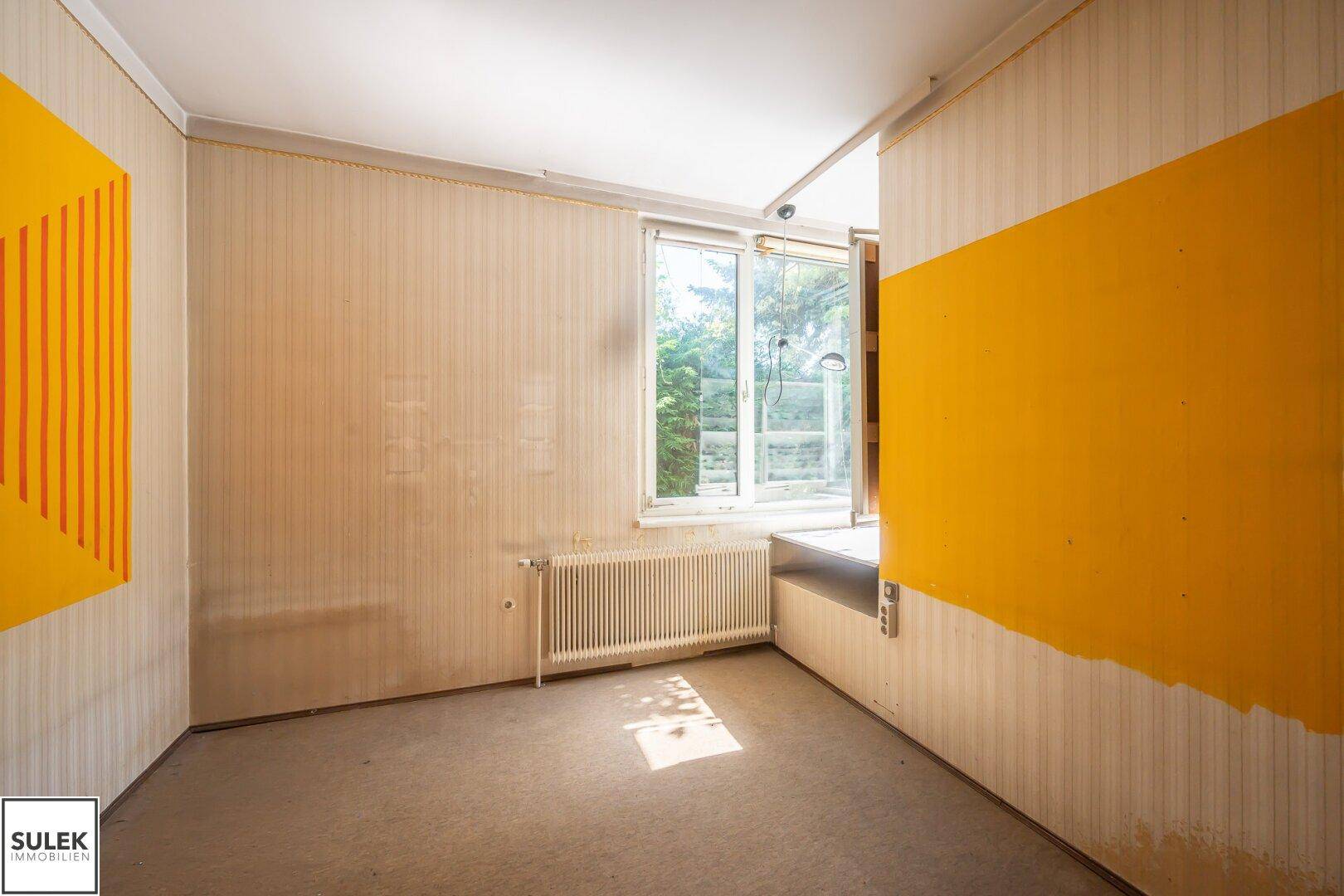 Schlafzimmer mit Fenster und Heizkörper, renovierungsbedürftig mit alter Tapete.