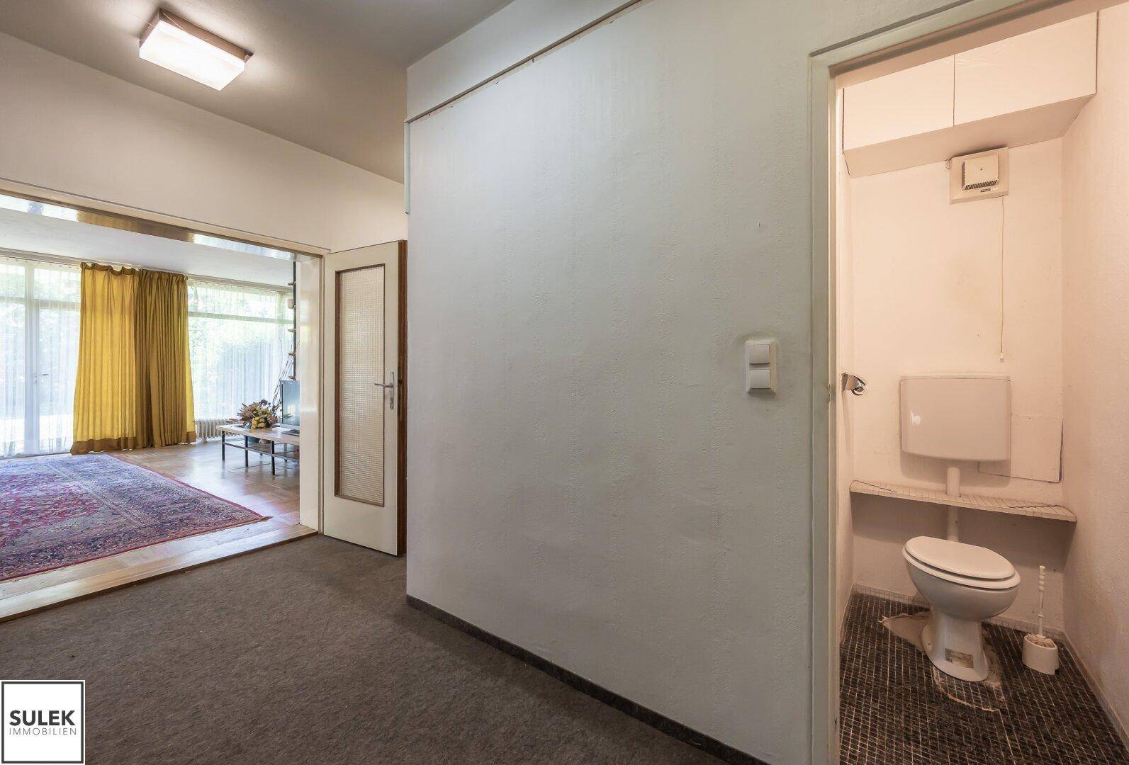 Ein Flur mit Teppichboden und Zugang zu einem Wohnzimmer sowie einer separaten Gästetoilette.
