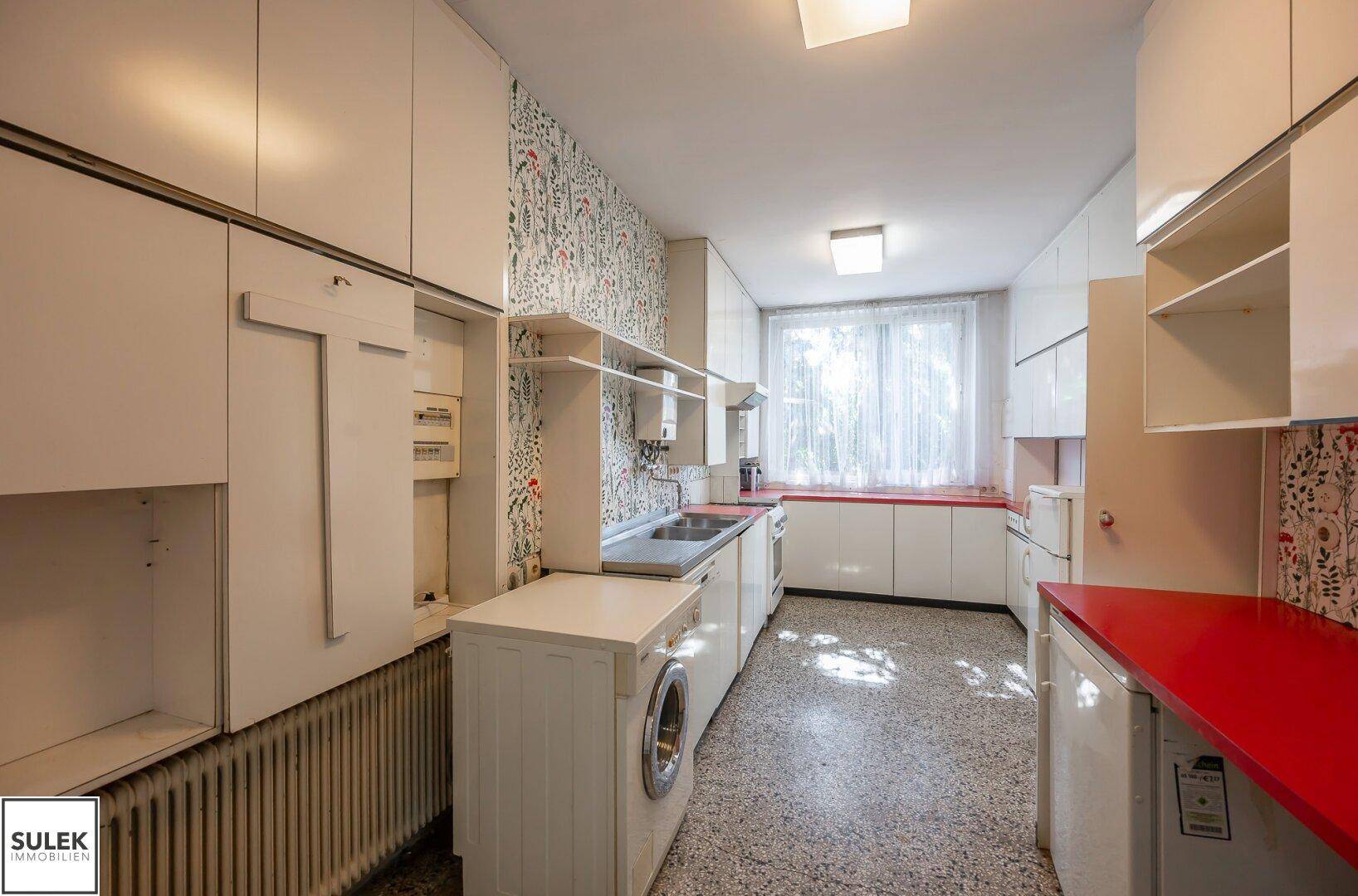 Eine Küche im Retro-Stil mit weißen Schränken, roten Arbeitsplatten und gemusterten Tapeten.