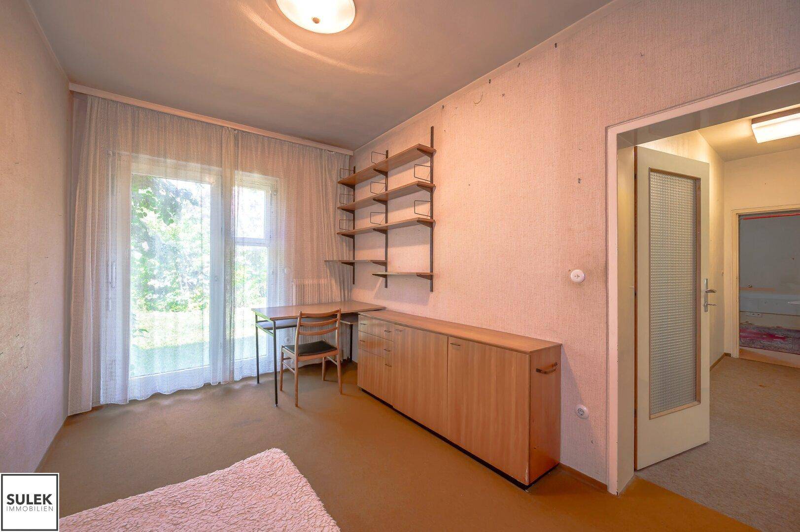 Helles Zimmer mit großem Fenster, Schrank und Regal, ideal als Schlaf- oder Arbeitszimmer mit Blick ins Grüne.