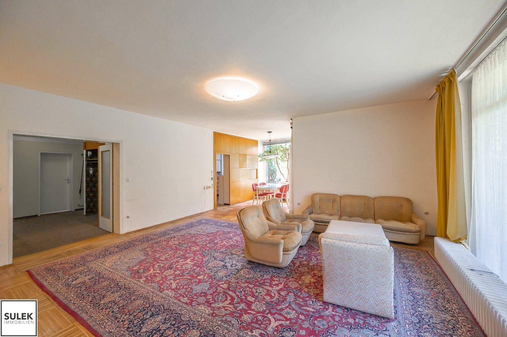 Geräumiger Wohnbereich mit Teppich und Zugang zu weiteren Räumen.