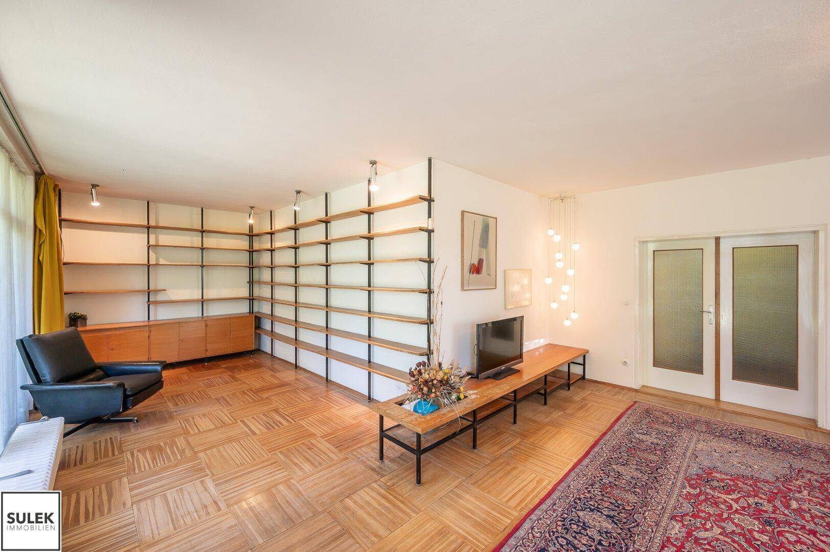 Geräumiges Wohnzimmer mit Parkettboden, Bücherregal und moderner Einrichtung.
