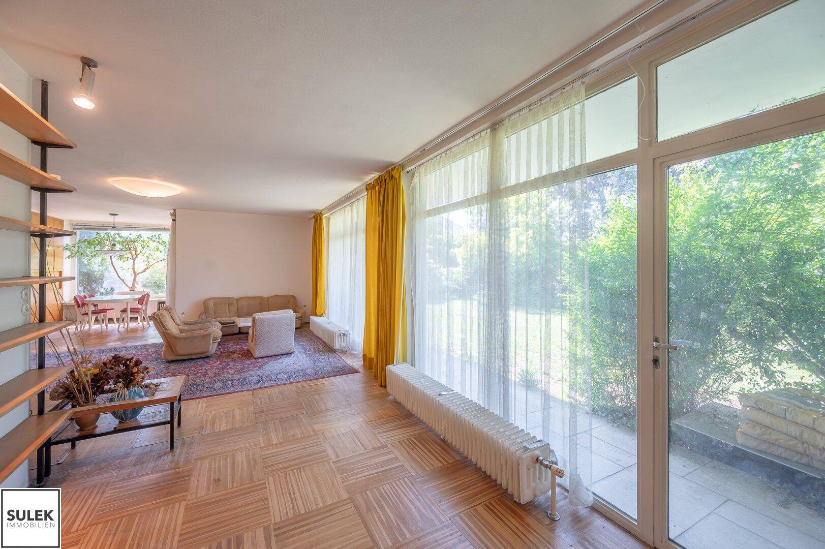 Helles Wohnzimmer mit Parkettboden, großen Fenstern und Blick ins Grüne.