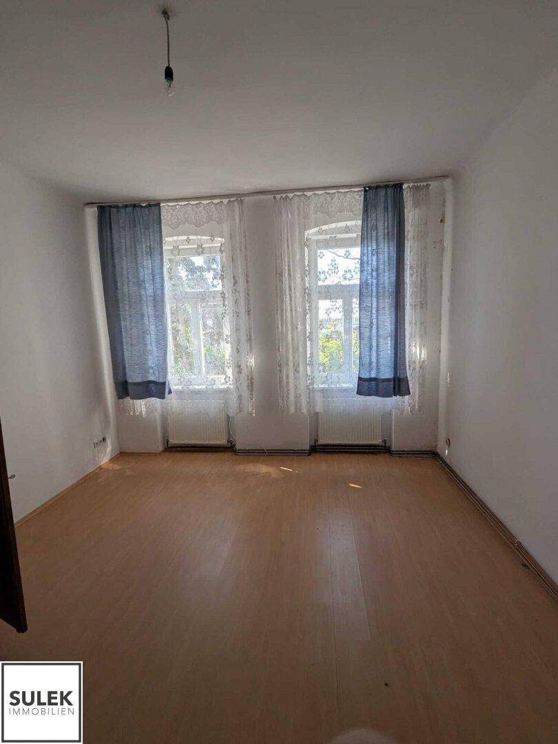 Helles Schlafzimmer mit Holzfußboden, zwei Fenstern und blauen Vorhängen.