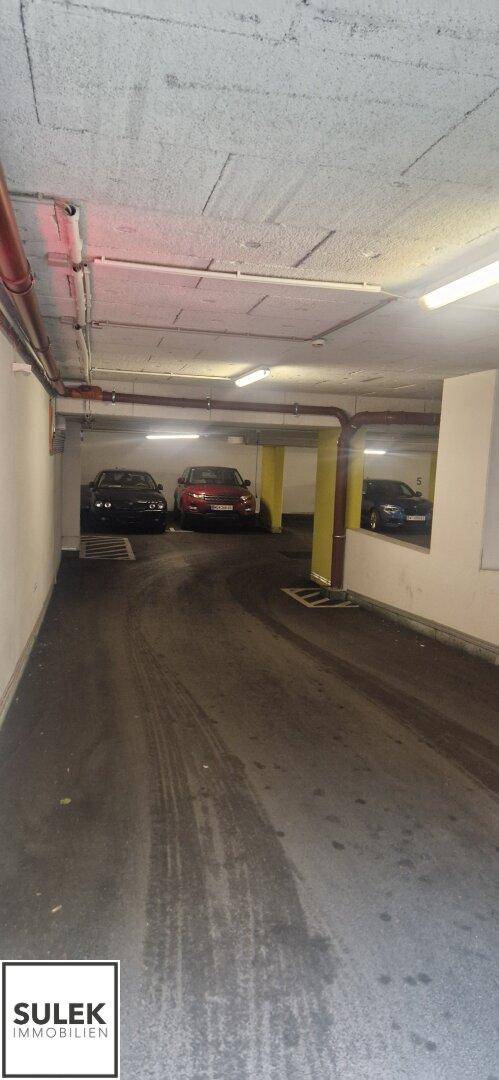 Geräumiger Gang in der Tiefgarage mit mehreren geparkten Fahrzeugen und Beleuchtung.