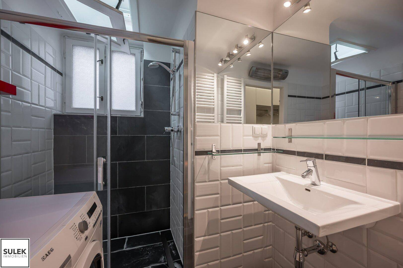 Modernes Badezimmer mit Dusche, Waschbecken und Waschmaschine, hell gefliest.