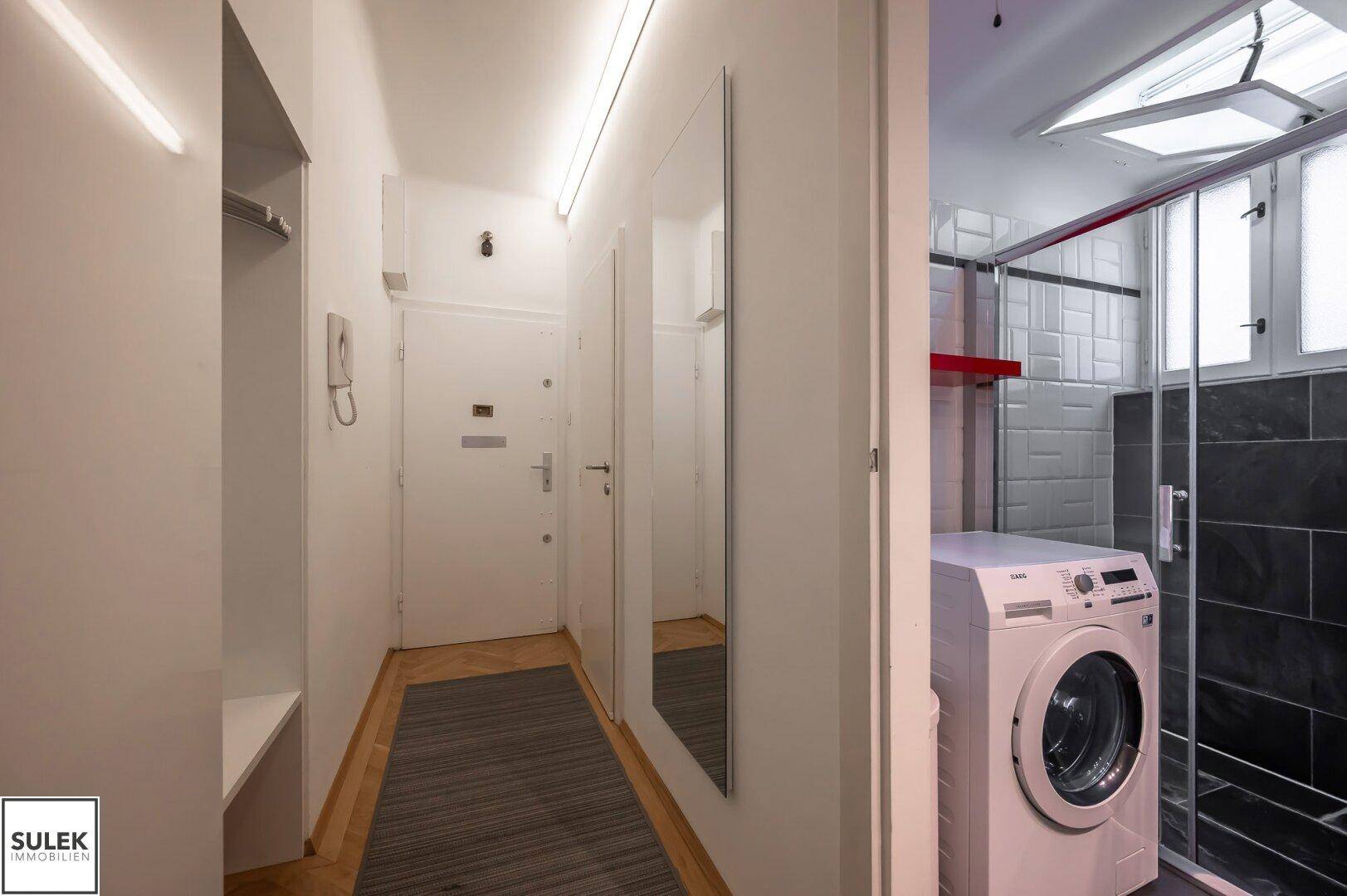 Eingangsbereich mit Garderobe und Blick in das angrenzende Badezimmer mit Dusche.
