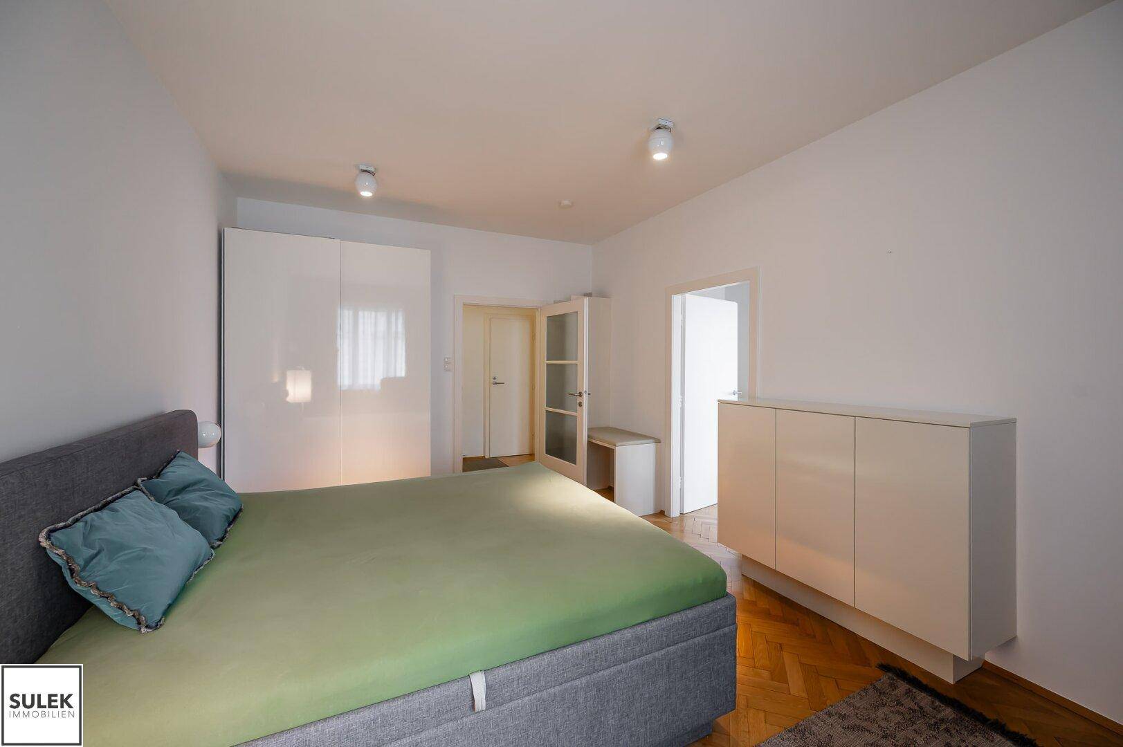 Geräumiges Schlafzimmer mit Doppelbett, weißen Schränken und Parkettboden.