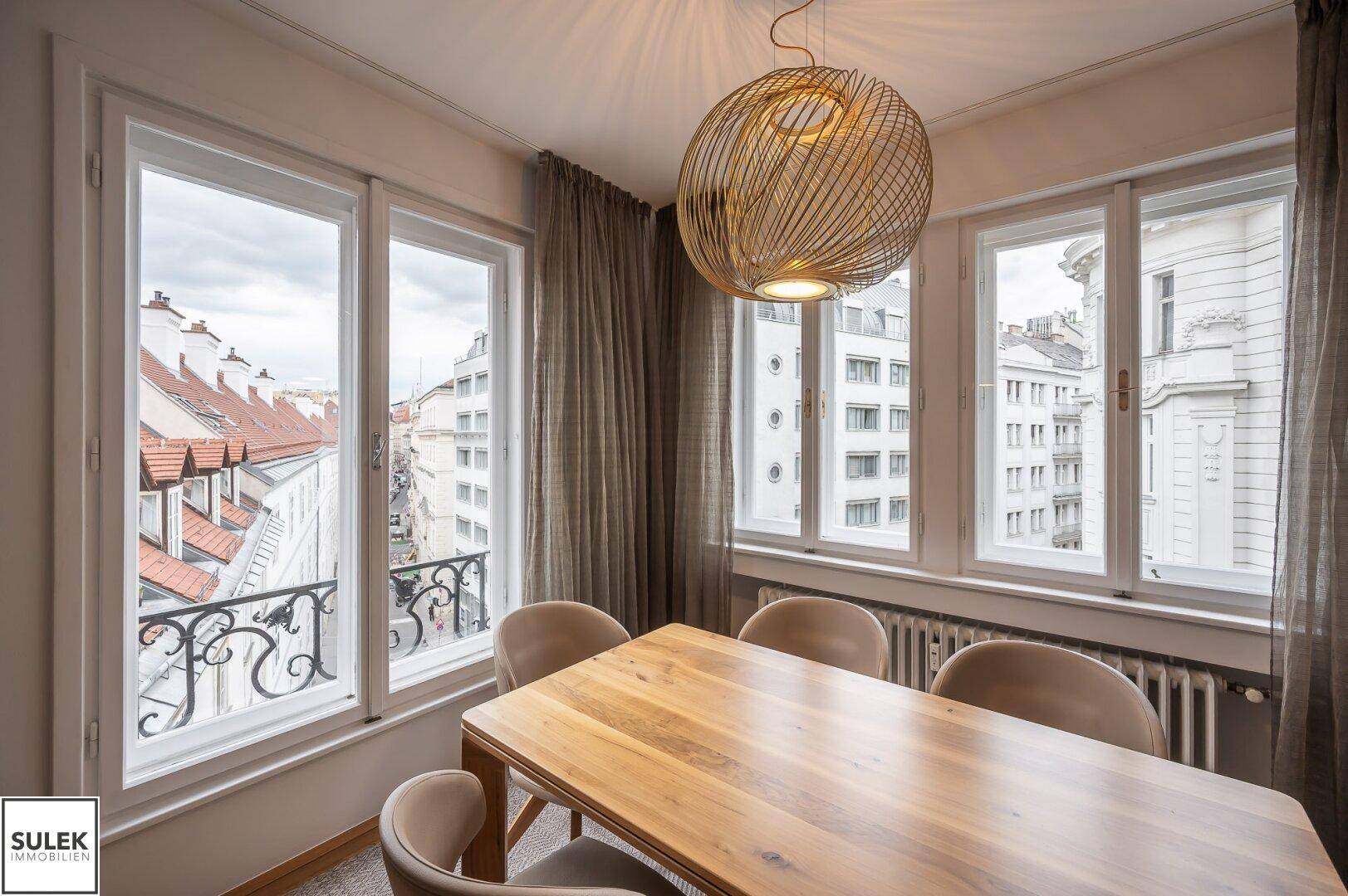 Gemütlicher Essbereich mit Holztisch, modernen Stühlen und Blick auf die Stadt durch große Fenster.