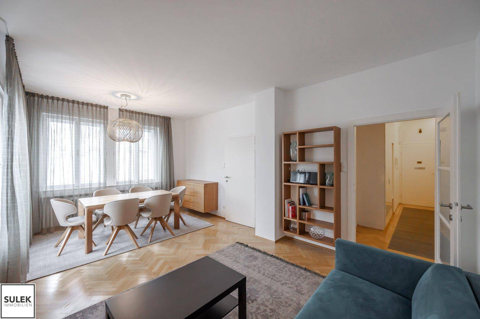 Geräumiger Wohn- und Essbereich mit Sofa, Esstisch und Bücherregal, verbunden mit anderen Räumen.