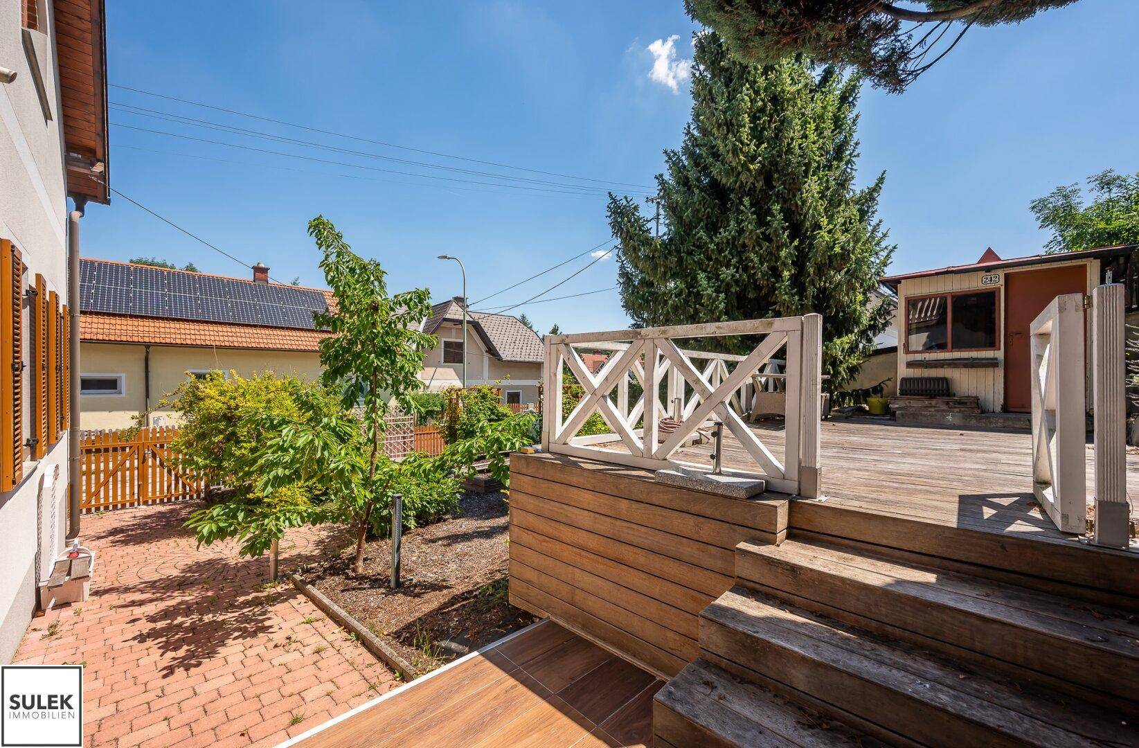 Holzterrasse mit Treppe und Blick auf den Garten sowie die umliegenden Häuser.