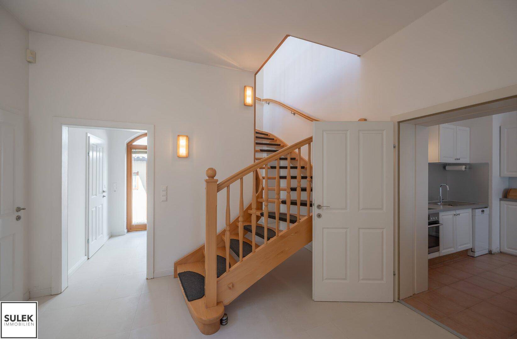Geräumiger Flur mit Holztreppe, die in die oberen Stockwerke führt, und Zugang zur Küche.