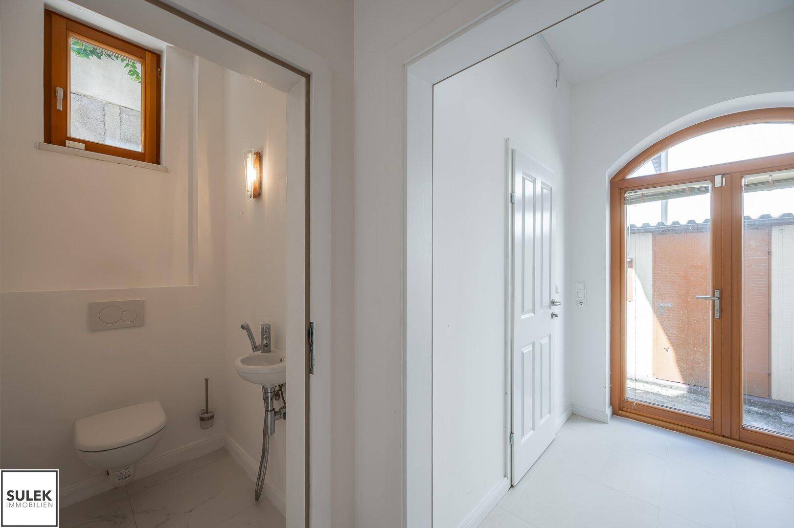Modernes Gäste-WC mit wandhängendem WC, kleinem Waschbecken und Fenster.