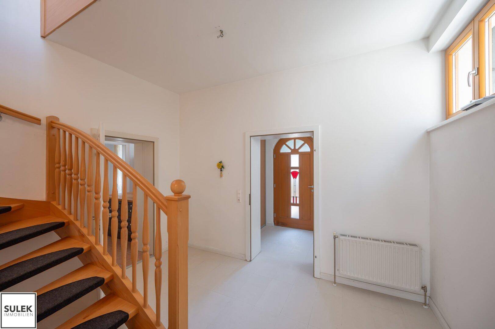 Heller Flur mit Holztreppe und Zugang zu verschiedenen Räumen im Erdgeschoss.