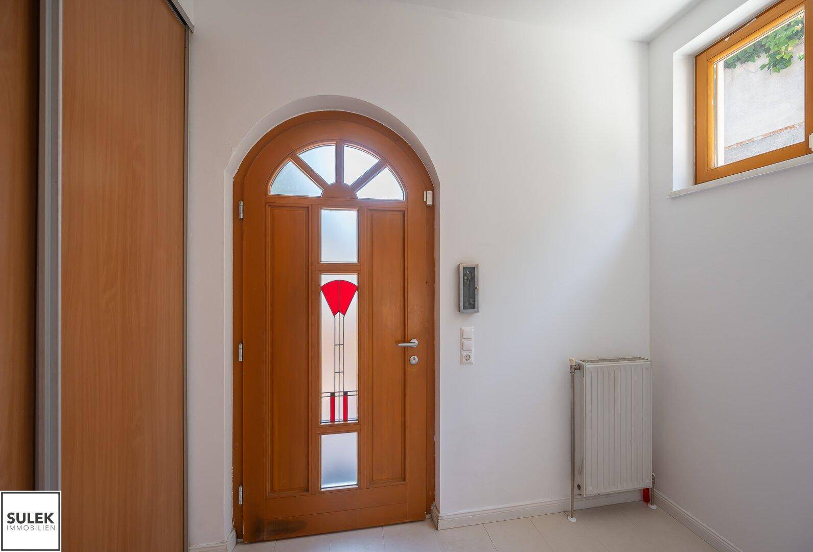 Heller Eingangsbereich mit Holztür, Fenster und integriertem Wandschrank.