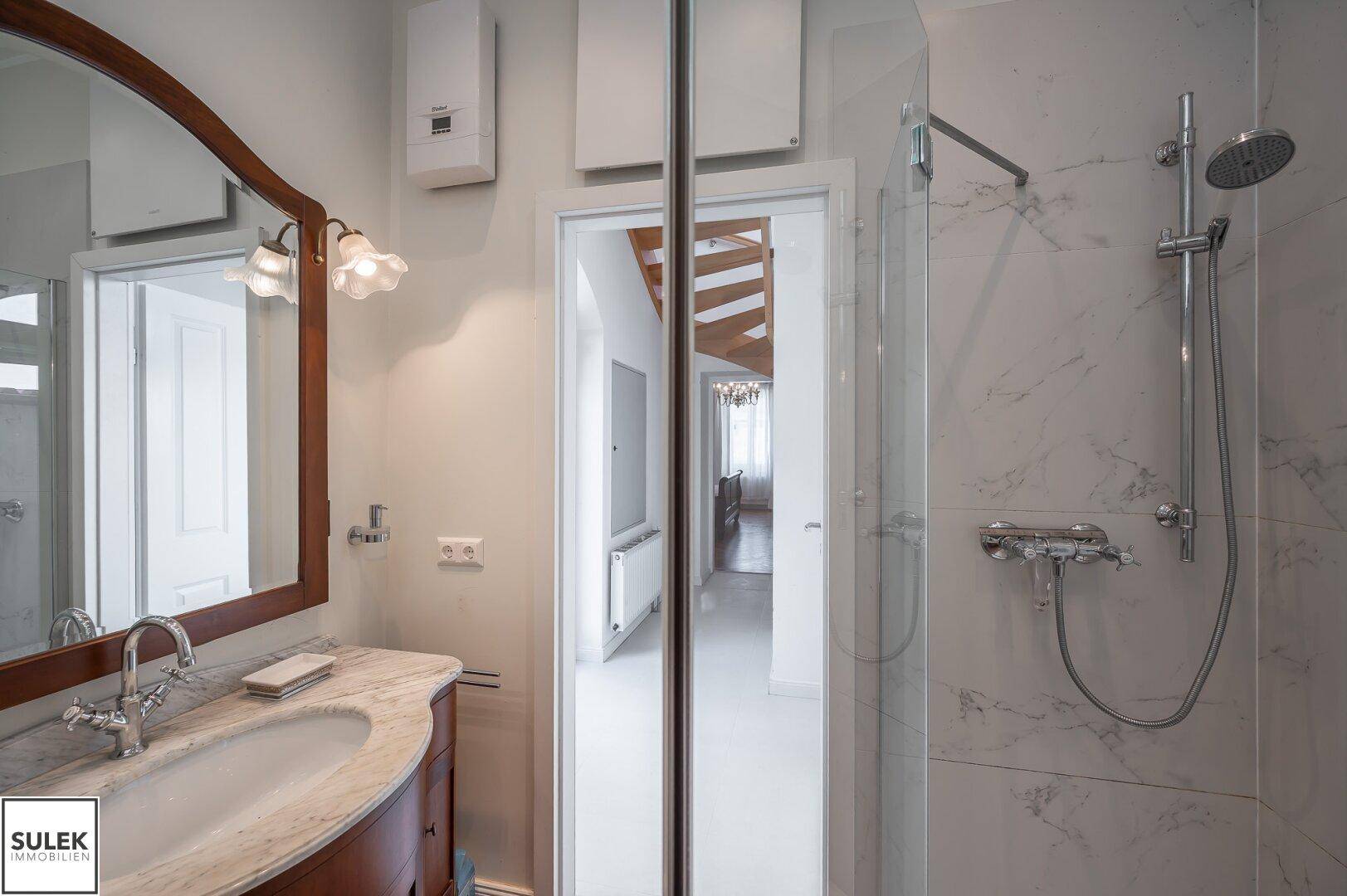 Modernes Badezimmer mit Marmorwaschtisch, Spiegel und Duschbereich mit Regendusche.