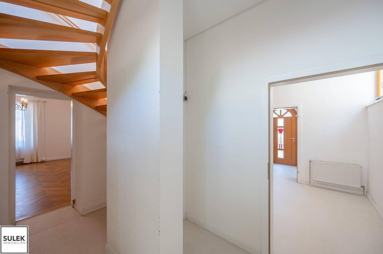 Flur mit Holztreppe und Blick auf den Eingangsbereich sowie angrenzende Zimmer.