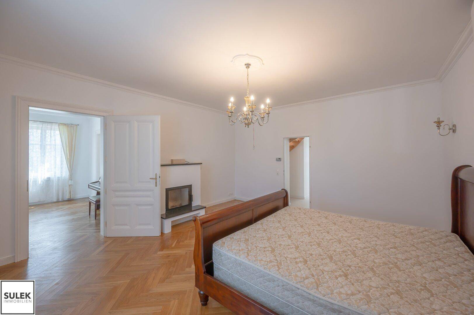 Helles Schlafzimmer mit Holzbett, Fischgrätparkett und Zugang zu einem weiteren Raum.