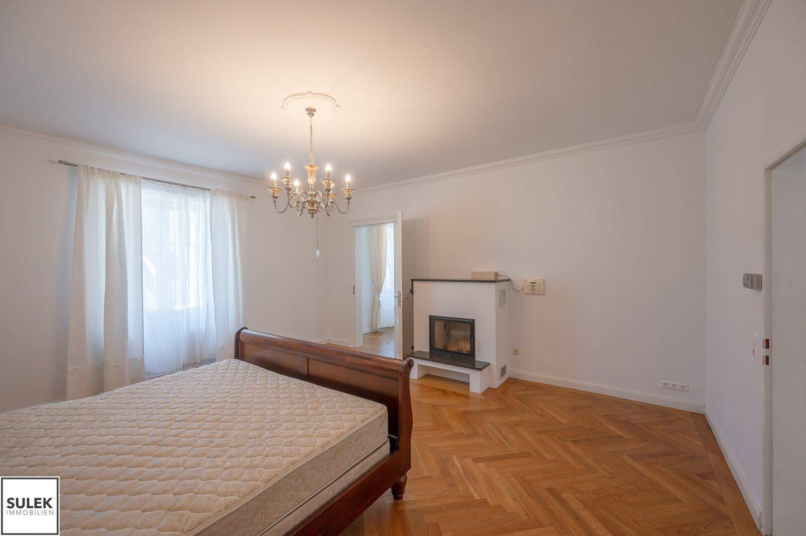 Schlafzimmer mit Holzbett, Fischgrätparkett und einem modernen Kamin.