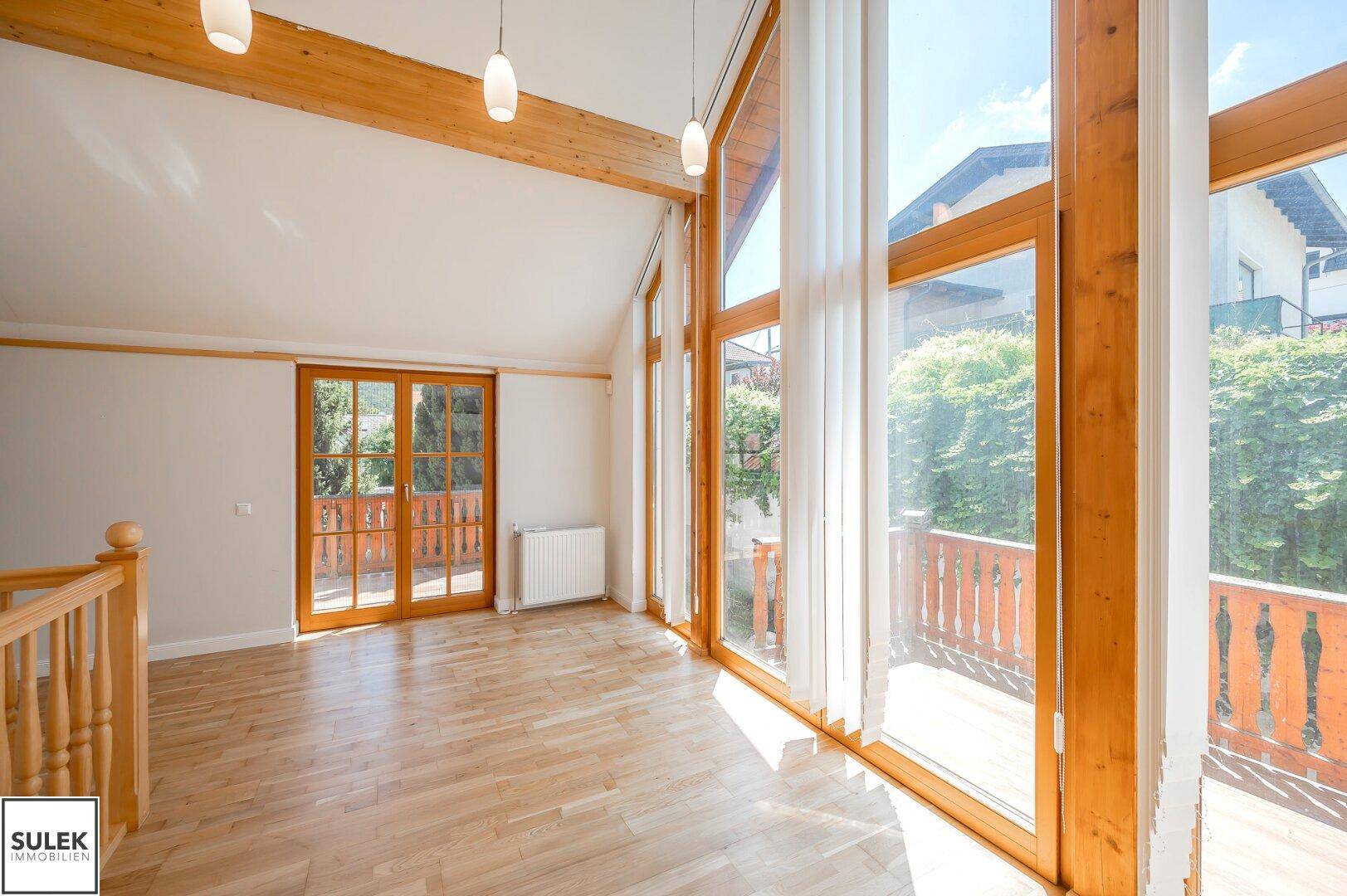 Lichtdurchfluteter Wohnbereich mit Holzboden, hohen Fenstern und Zugang zu einem Balkon.