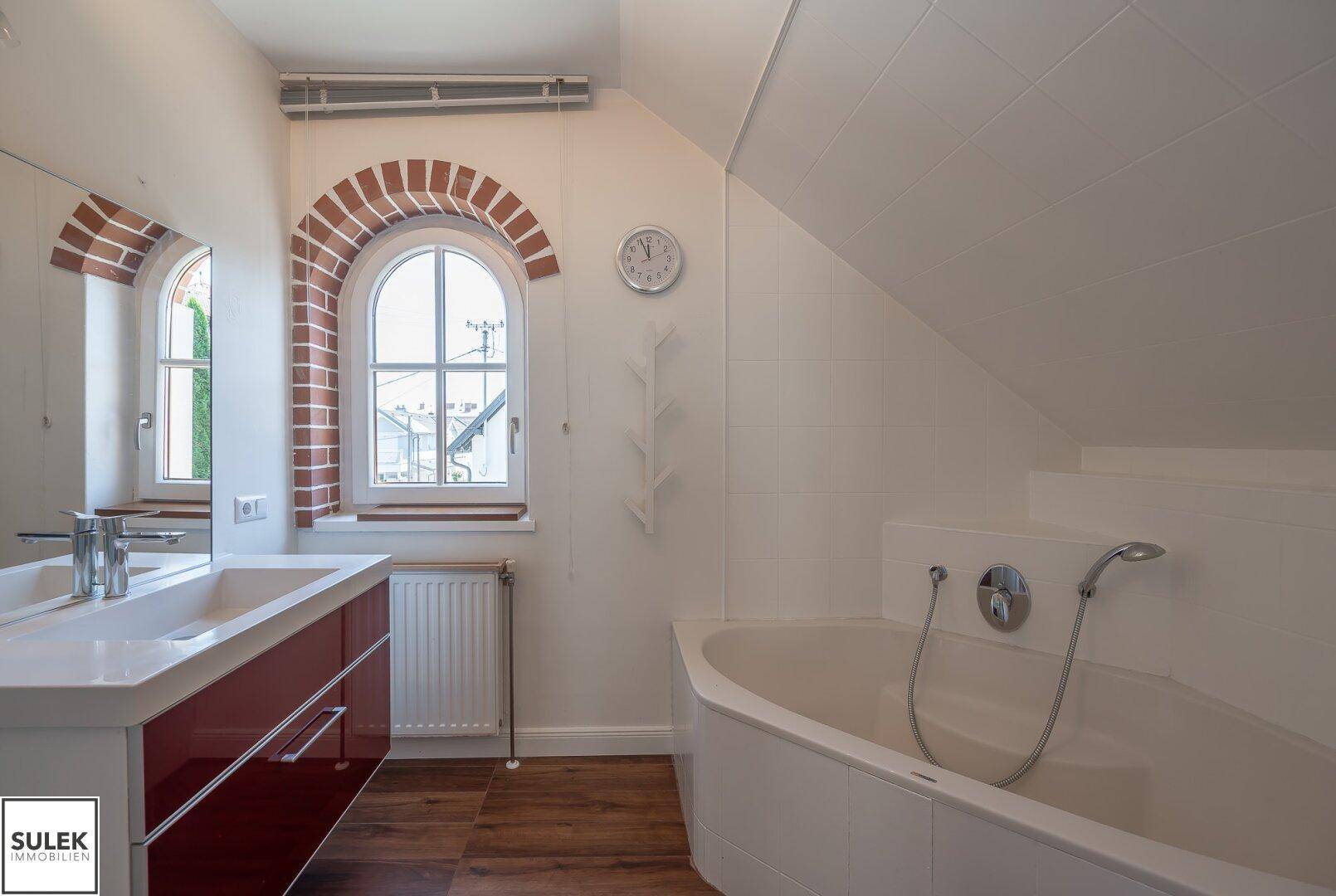 Badezimmer mit Badewanne, modernem Waschtisch und Fenster mit Ziegelbogen.