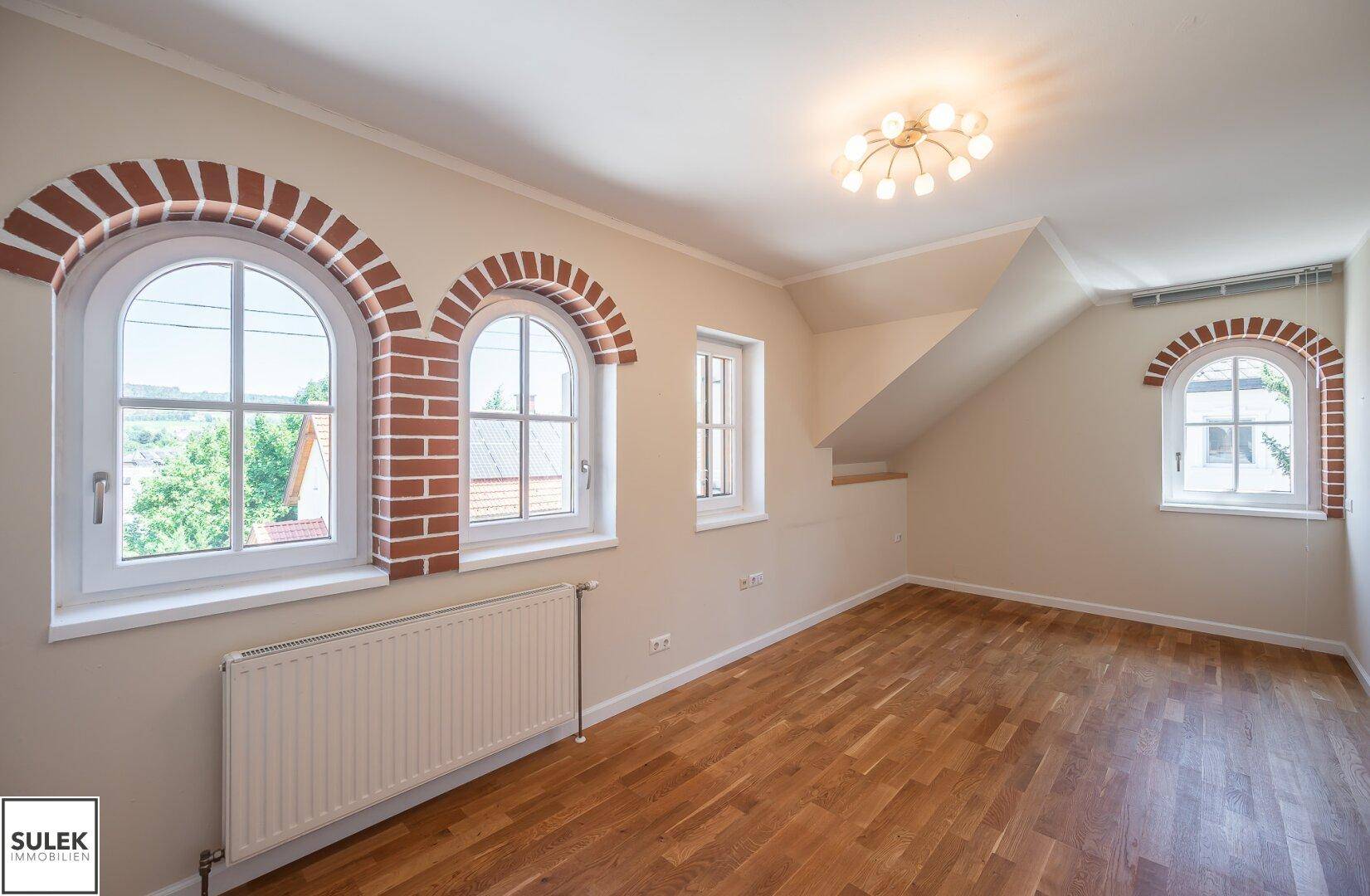 Helles Schlafzimmer mit Holzboden, charmanten Rundbogenfenstern und Dachschrägen.