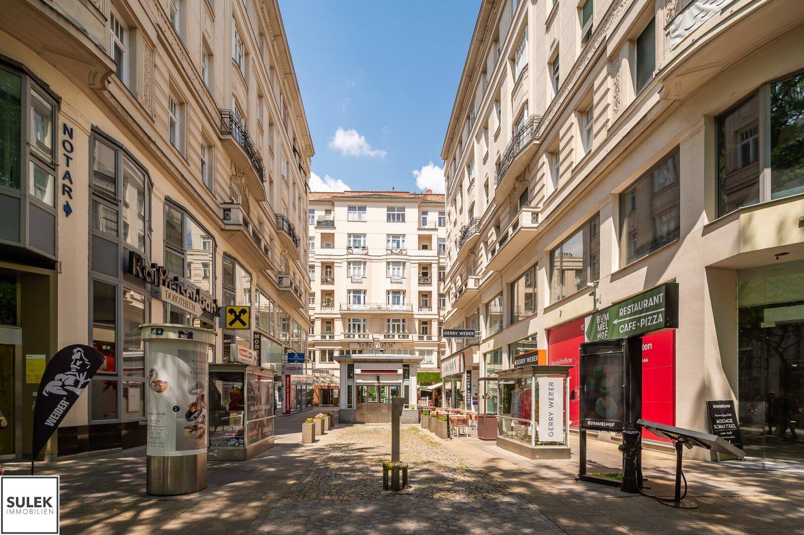 Historische Einkaufsstraße mit Geschäften und Restaurants, umgeben von klassischen Gebäudefassaden.