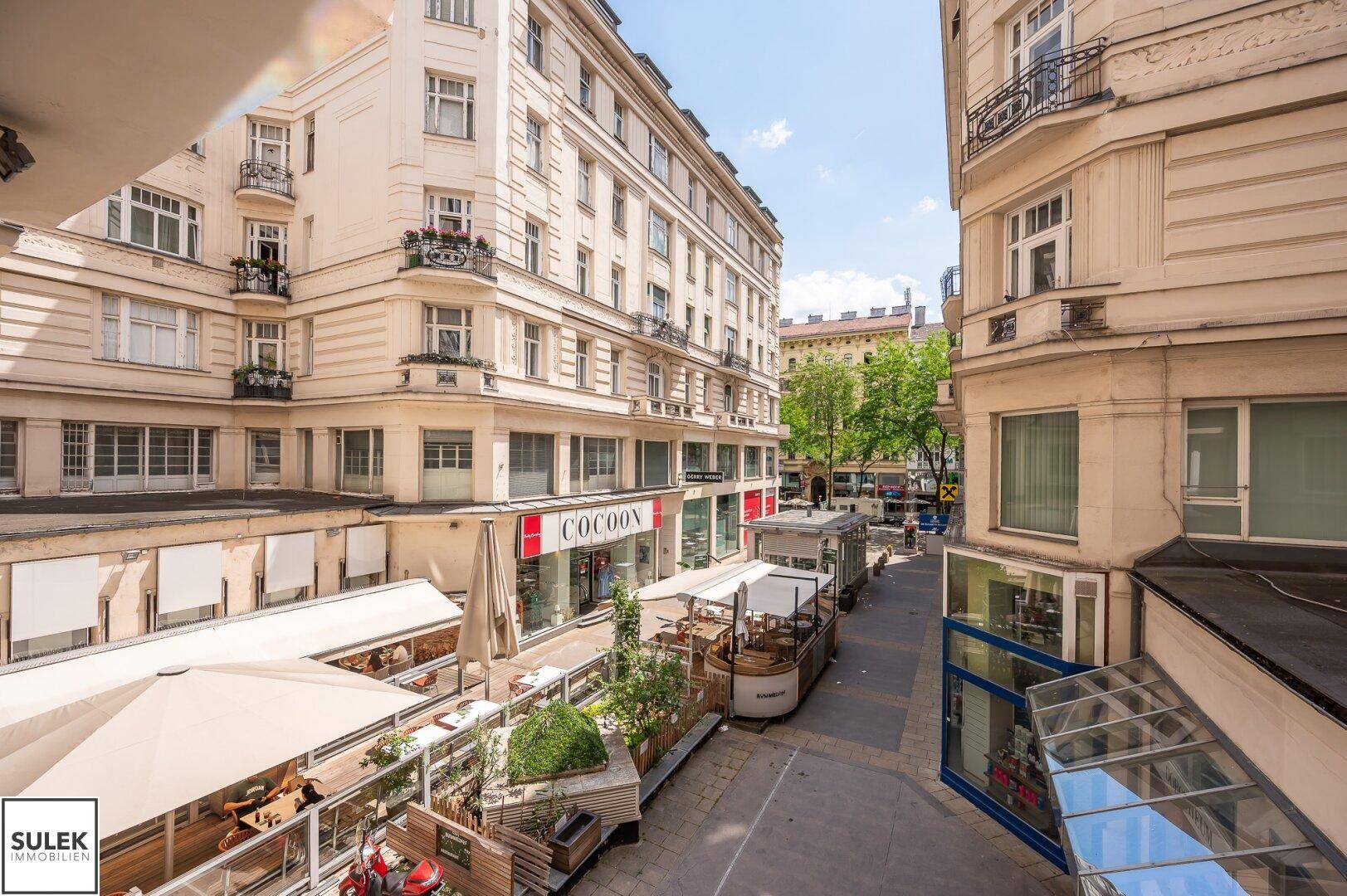 Blick von oben auf eine belebte Gasse mit Geschäften, Restaurants und historischen Gebäuden.