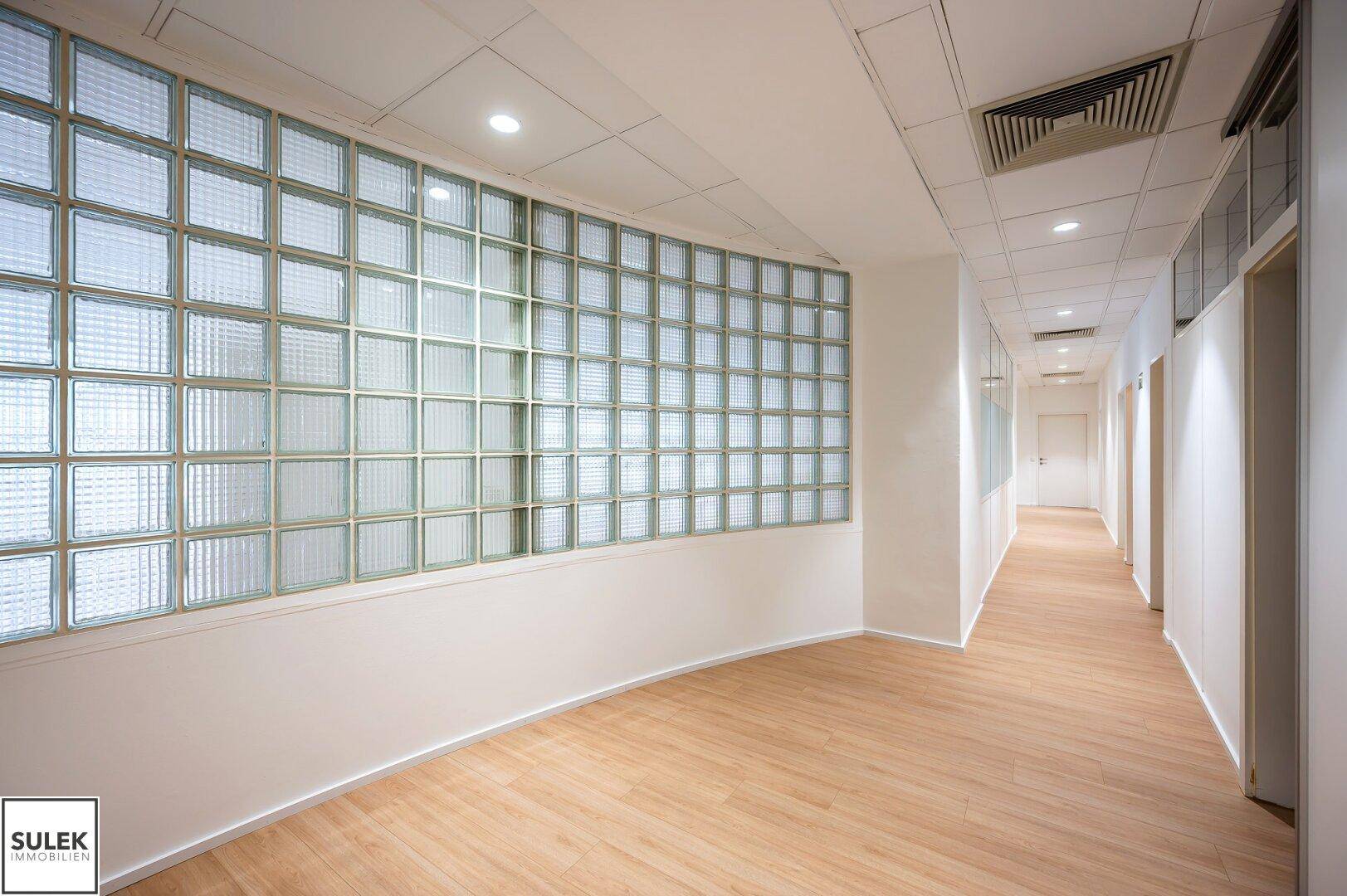 Moderner Bürogang mit einer Wand aus Glasbausteinen, die für natürliches Licht sorgt.